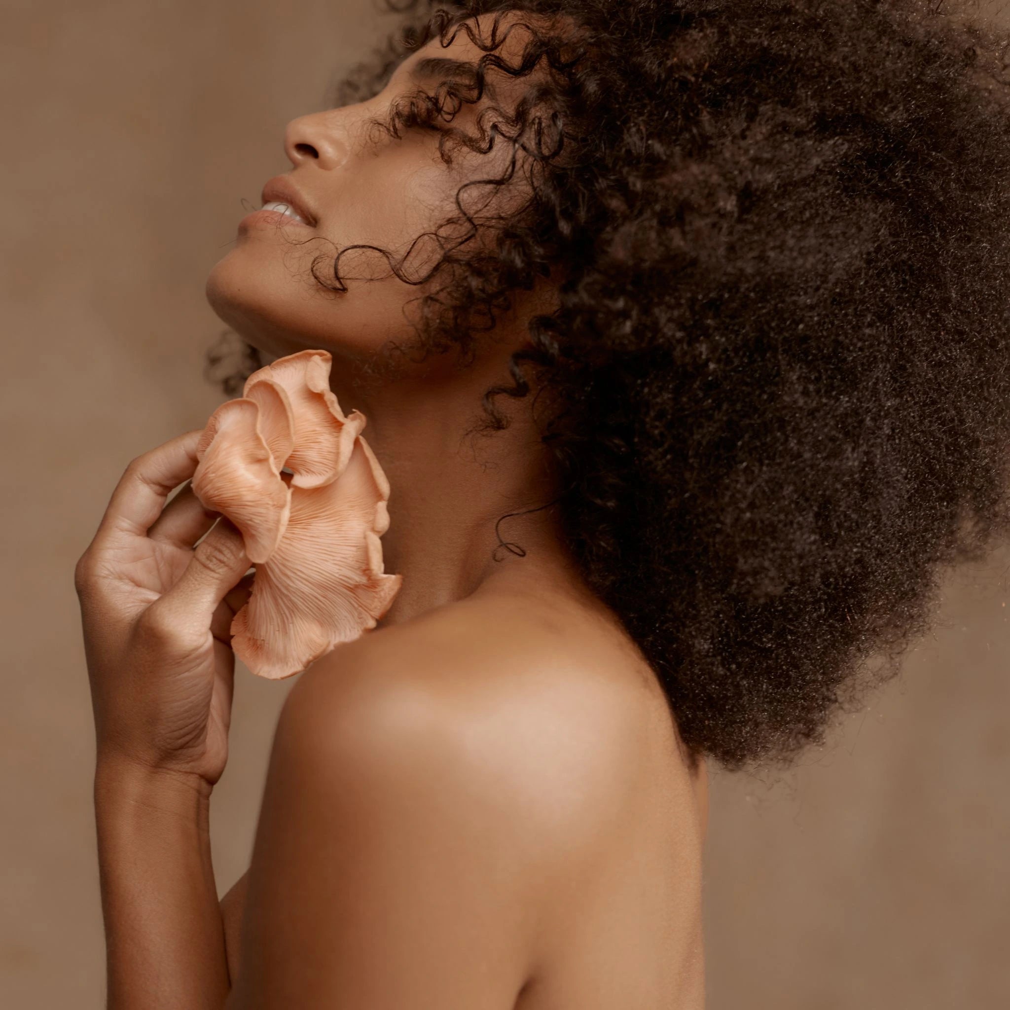 Side profile of a woman smiling and holding fresh oyster mushrooms near her face, embodying the connection between beauty, wellness, and Mother Made mushrooms.