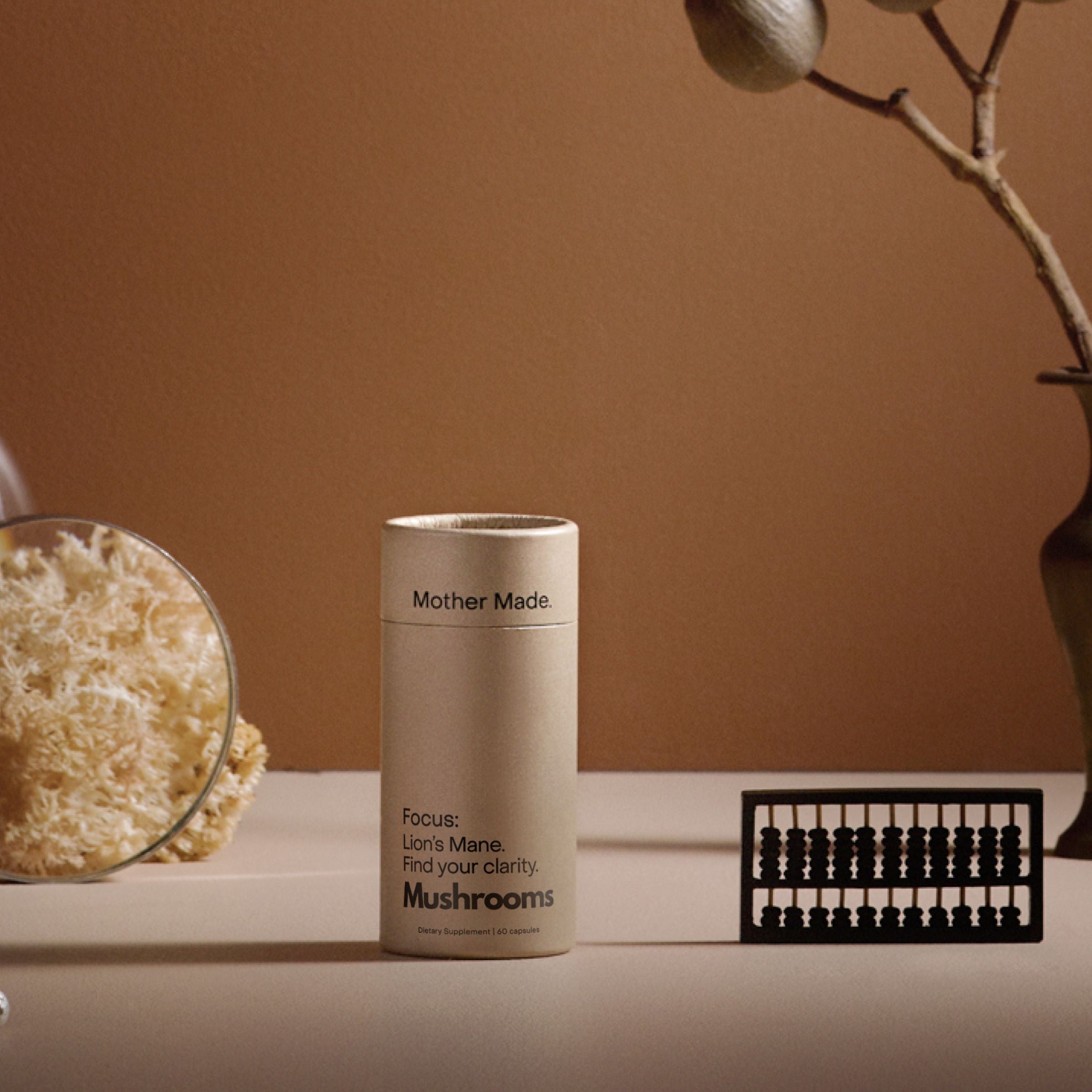 Mother Made Focus Lion’s Mane mushroom supplement in BPA-free recyclable packaging, styled with dried botanicals and magnified Lion’s Mane.