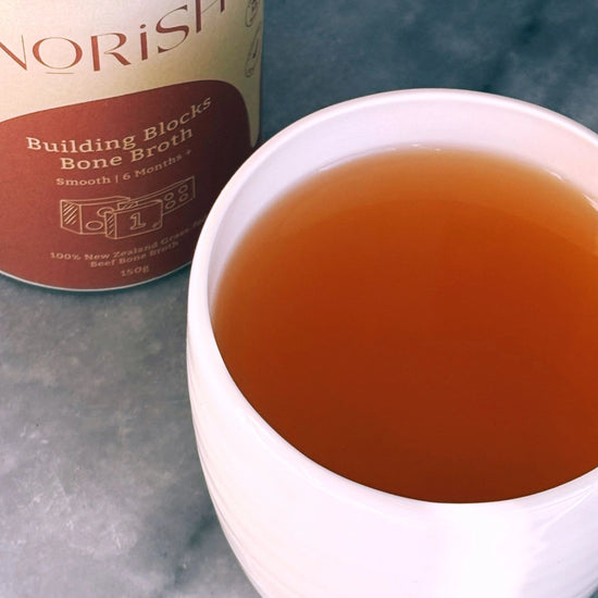 A warm cup of Norish Building Blocks Bone Broth with its packaging in the background