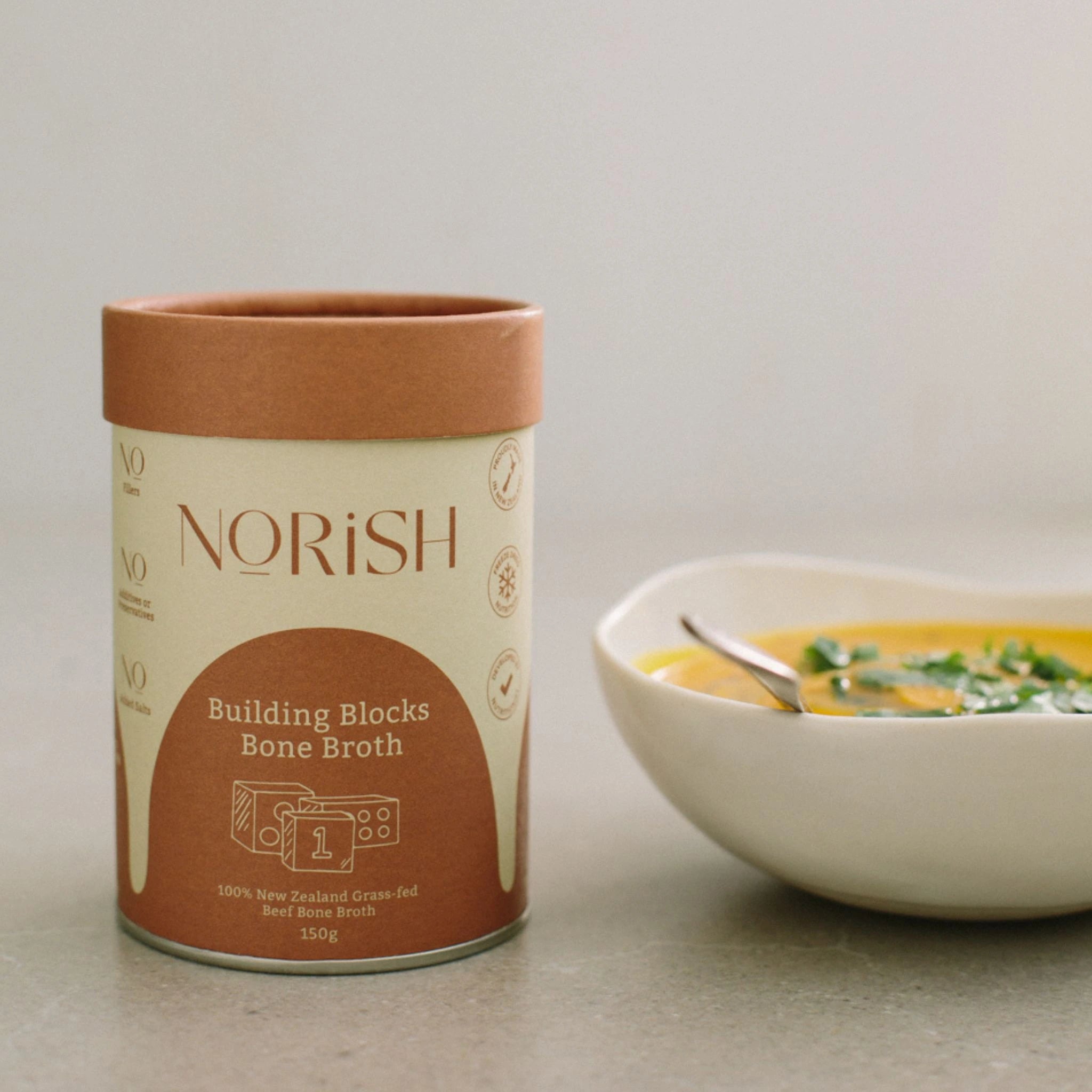 Norish Building Blocks Bone Broth 150g beside a bowl of nourishing soup
