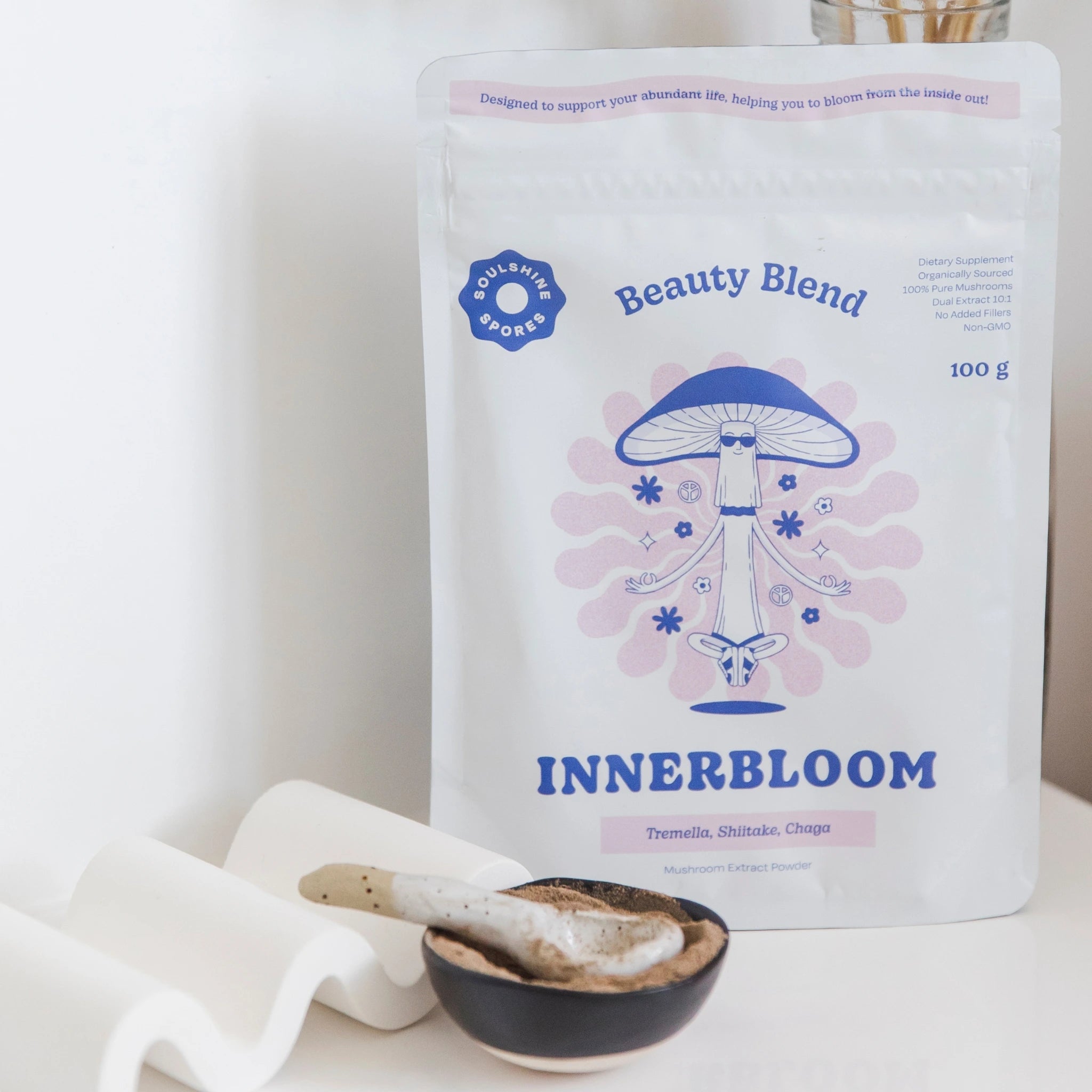 A pouch of Soulshine Spores InnerBloom Beauty Blend, a 100% organic medicinal mushroom powder in a bowl with spoon featuring 100% organic Tremella, Shiitake, and Chaga
