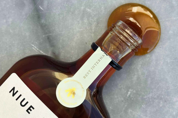 Niue Honey bottle with honey spilling onto marble, showing its Best International Honey award tag