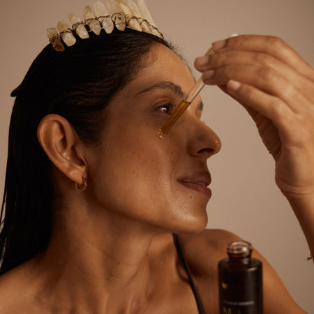 Woman applying facial oil with a dropper, using Vanessa Megan skincare. Wearing a crystal crown.