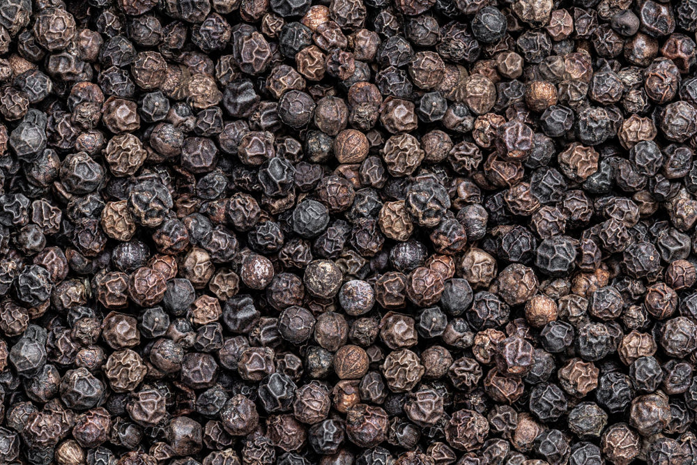 Close-up of whole black peppercorns (Piper Nigrum), a warming botanical prized for its spicy, energising top note and antioxidant-rich skincare, wellness and health benefits.