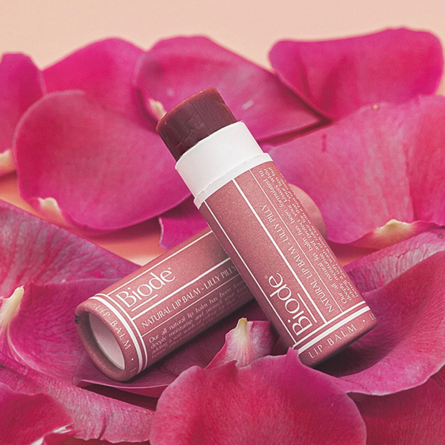 Biode tinted natural lip balm in Lilly Pilly shade surrounded by pink petals for soft lip care