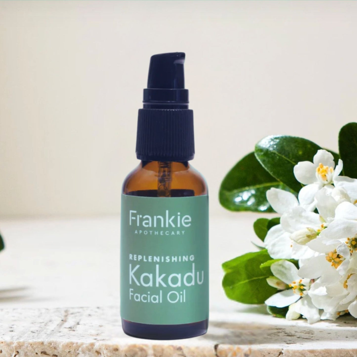 Frankie Apothecary Replenishing Kakadu Facial Oil in an amber glass bottle displayed beside white botanical blossoms and green leaves.