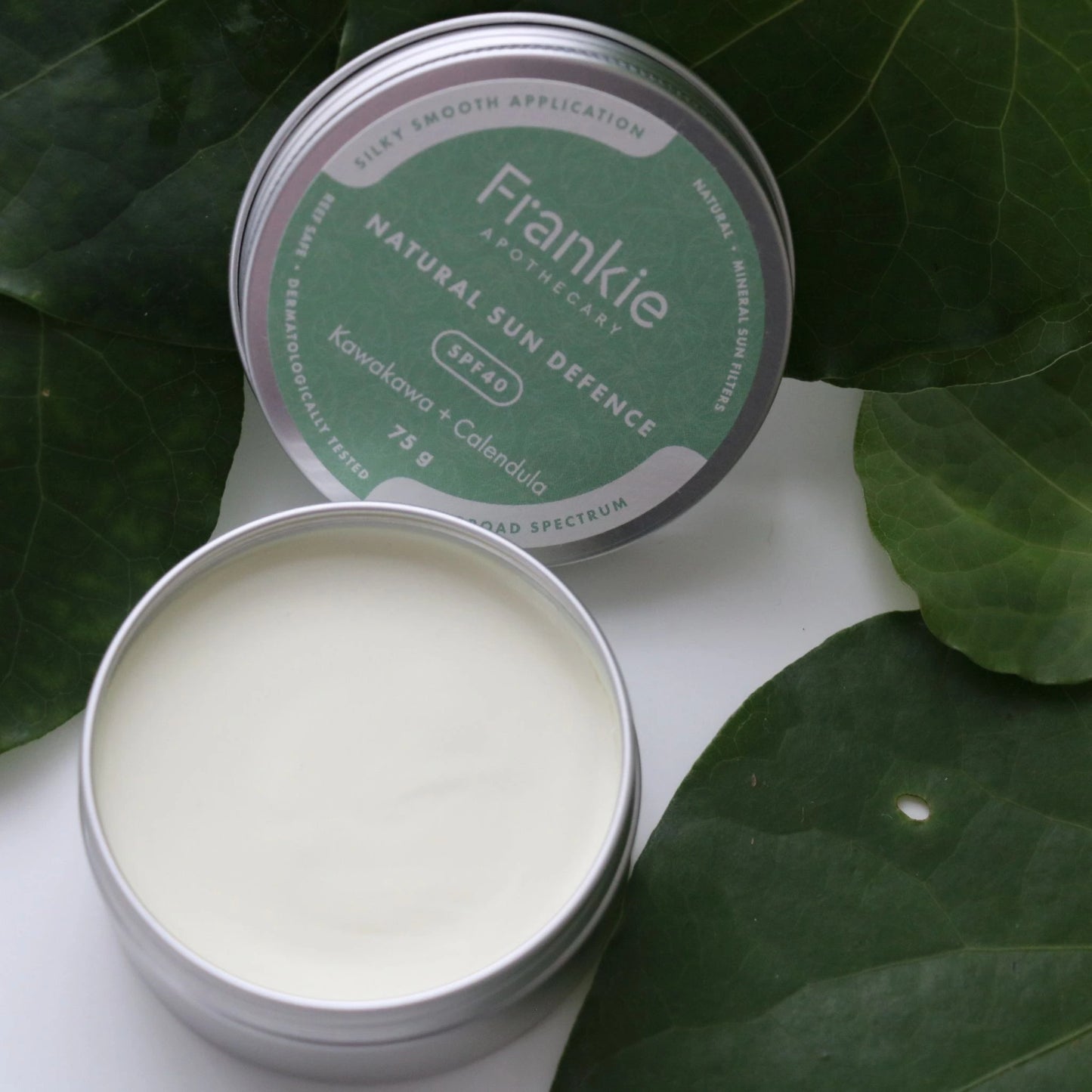 Frankie Natural Sun Defence SPF40 open tin resting on kawakawa leaves – mineral sunscreen with soothing botanical actives.