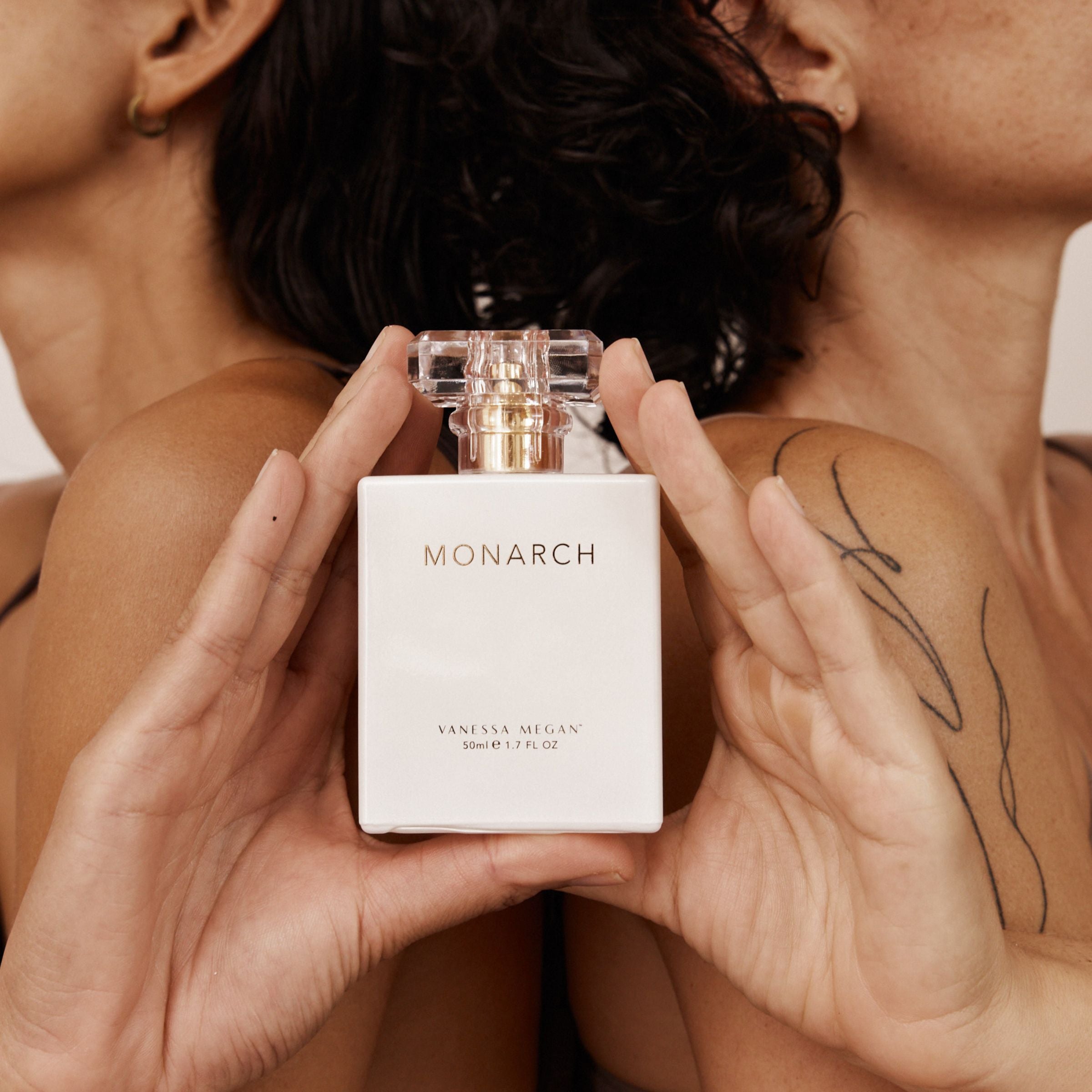 Vanessa Megan Monarch Perfume held between two women with bare shoulders, highlighting the bottle’s size and design.