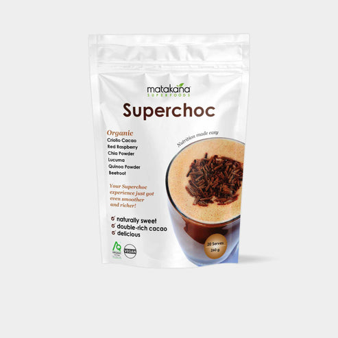 A stand-up pouch of Matakana Superchoc Organic criollo cacao drinking powder superfood blend on a light gray background. The white pouch features brown and green text, a photo of a frothy Superchoc drink topped with dark cocoa powder and a small green organic certification logo near the bottom left.
