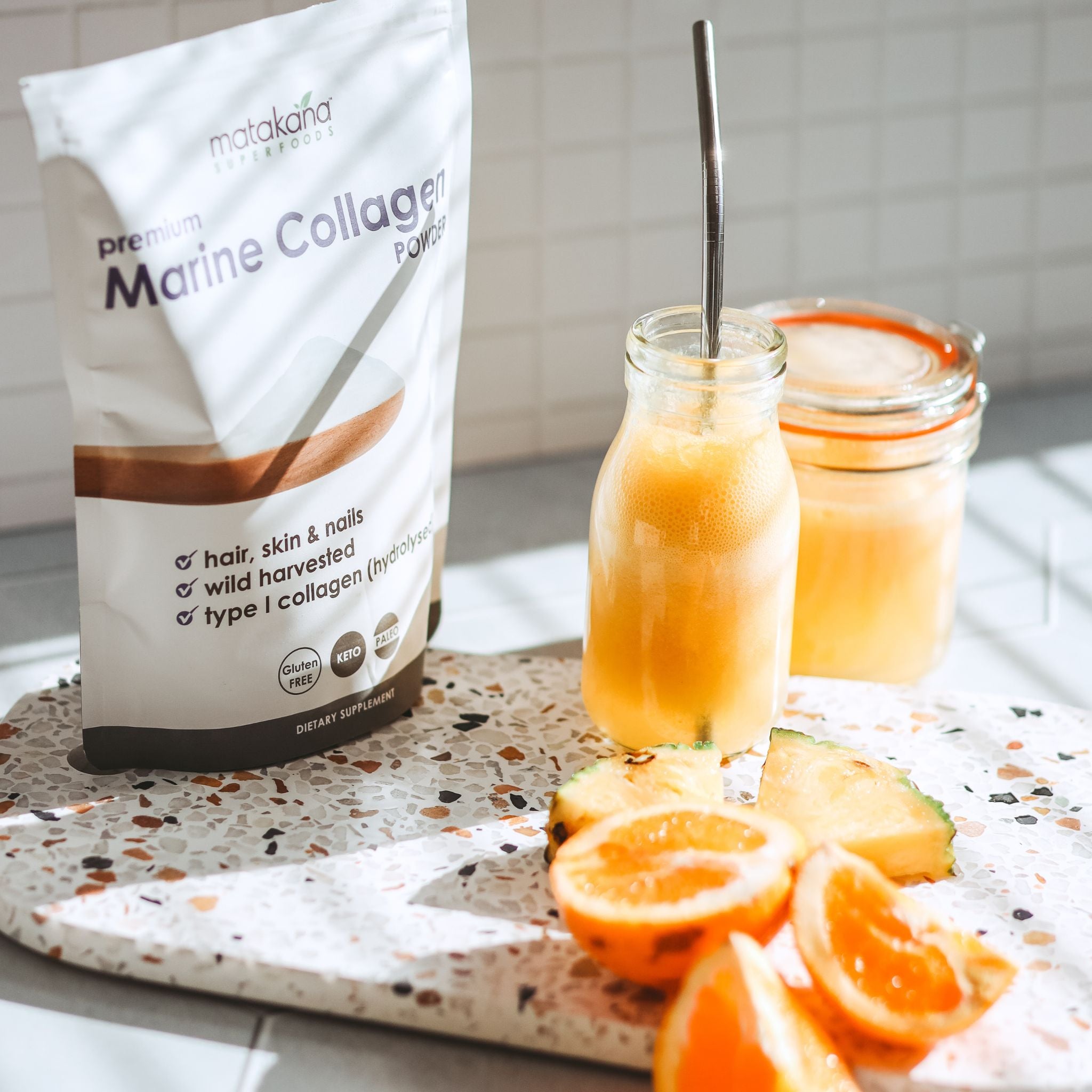  Matakana Superfoods Marine Collagen Powder pouch lifestyle shot  with freash cut pineapple, citrus and juice on bench.