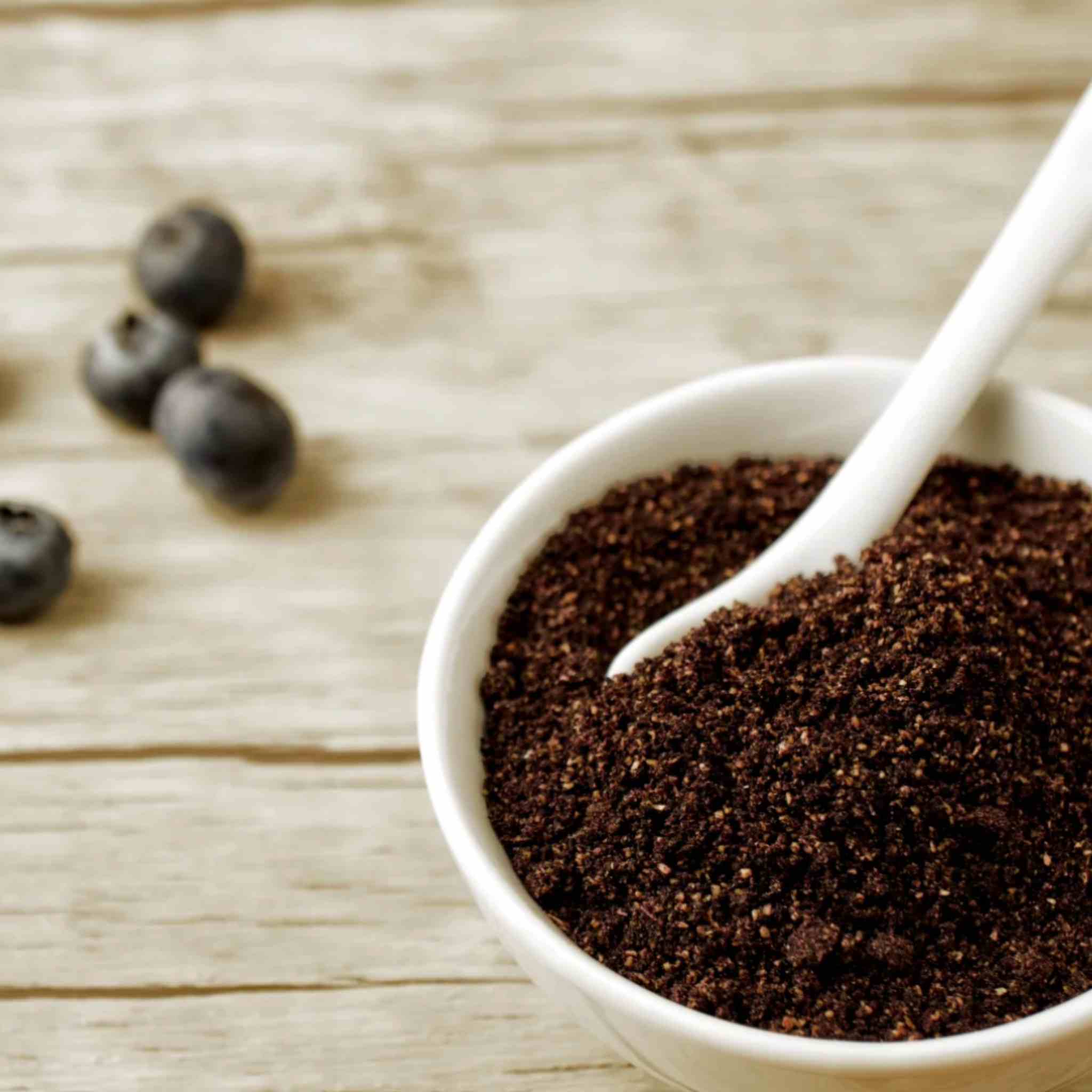 A white bowl filled with the Matakana organic Maqui berry powder, with a white spoon resting inside and a few berries on a light wooden surface in the background.
