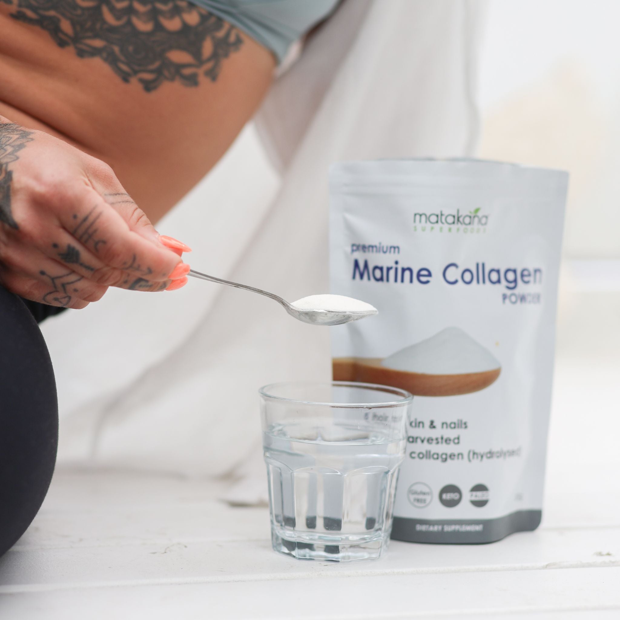 Women adding Matakana Superfoods Premium Marine Collagen Peptide Powder to glass of water with pouch in background.