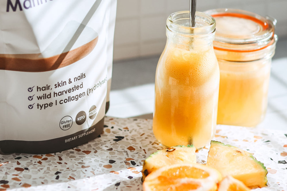 Lifestyle shot of the Matakana Superfoods Premium Marine Collagen Peptide Powder pouch with fresh cut pineapple, citrus and juice in glass bottle on countertop.
