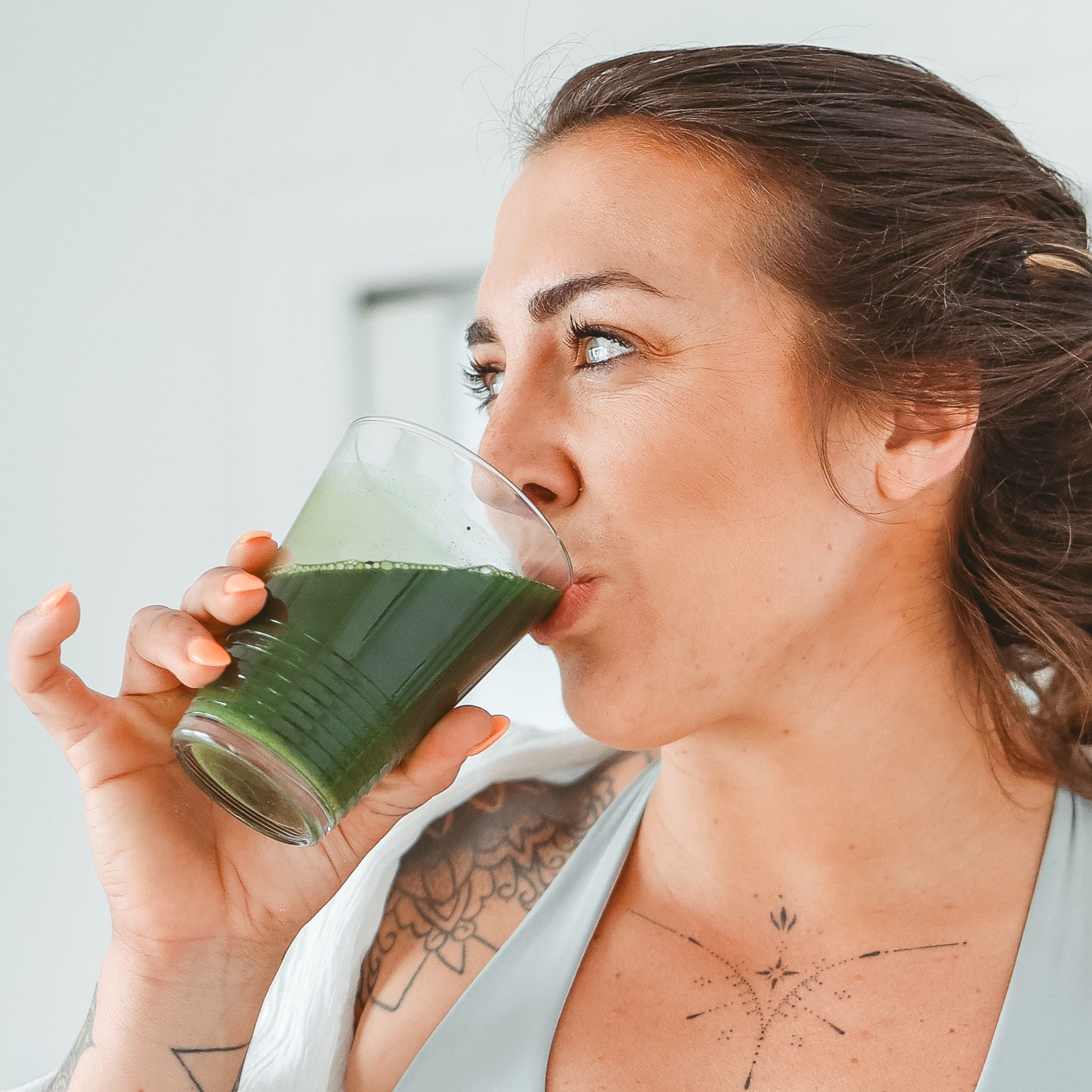 Women enjoying drinking her Matakana Superfoods Supergreens from glass  in sunlit room.