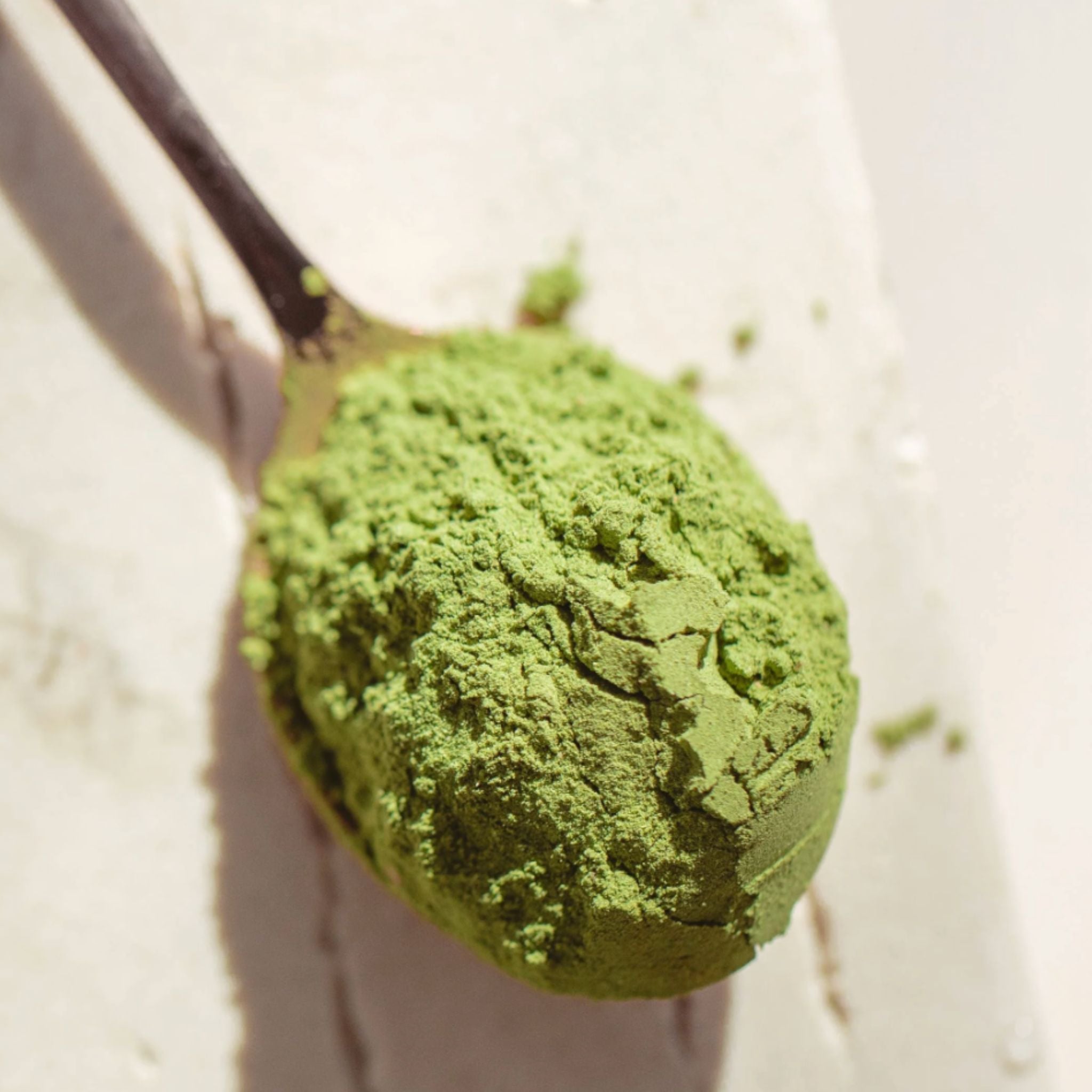 Close up shot of the Matakana Superfoods Supergreens Biome Powder on a spoon on marble surface.