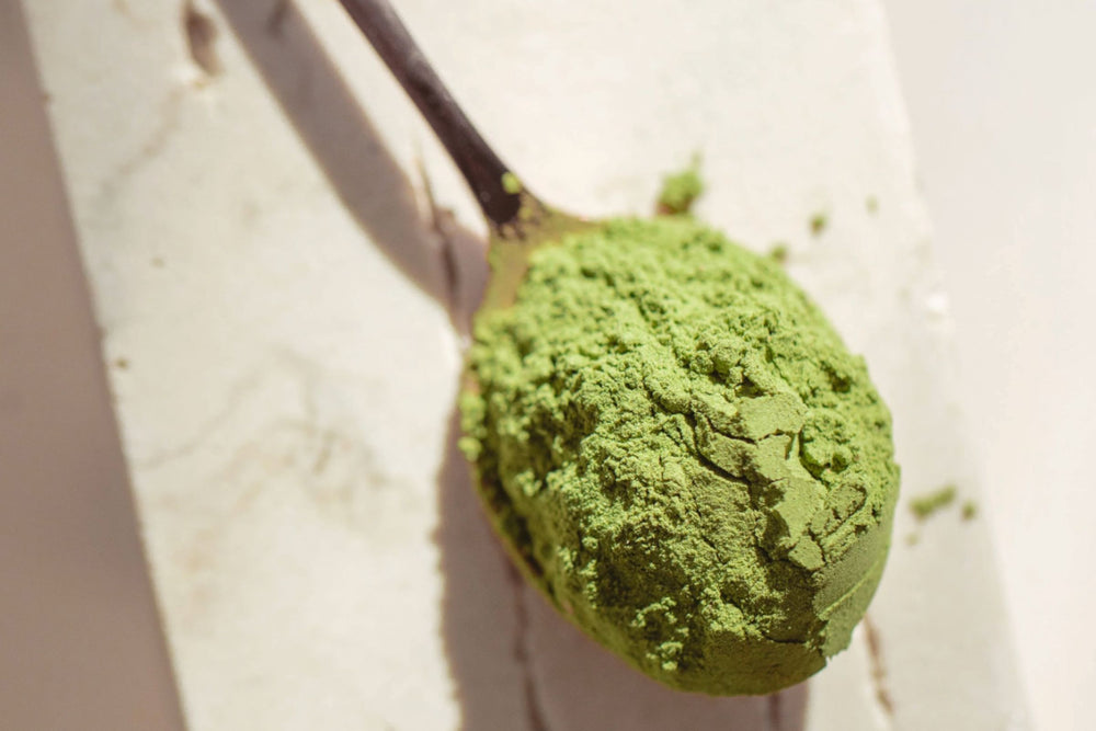 Spoon full of the Matakana Superfoods Supergreens Biome Powder shot on a marble surface in natural light.