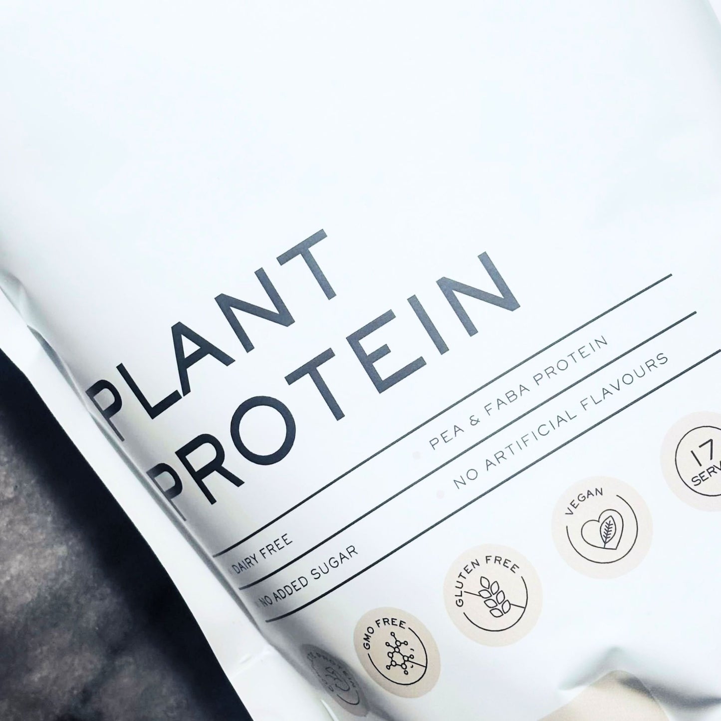 A close-up of the Matakana Superfoods Unflavoured plant-based protein powder pouch with bold black text reading 'PLANT PROTEIN' and small circular badges indicating dietary, gluten-free, vegan, and serving information.