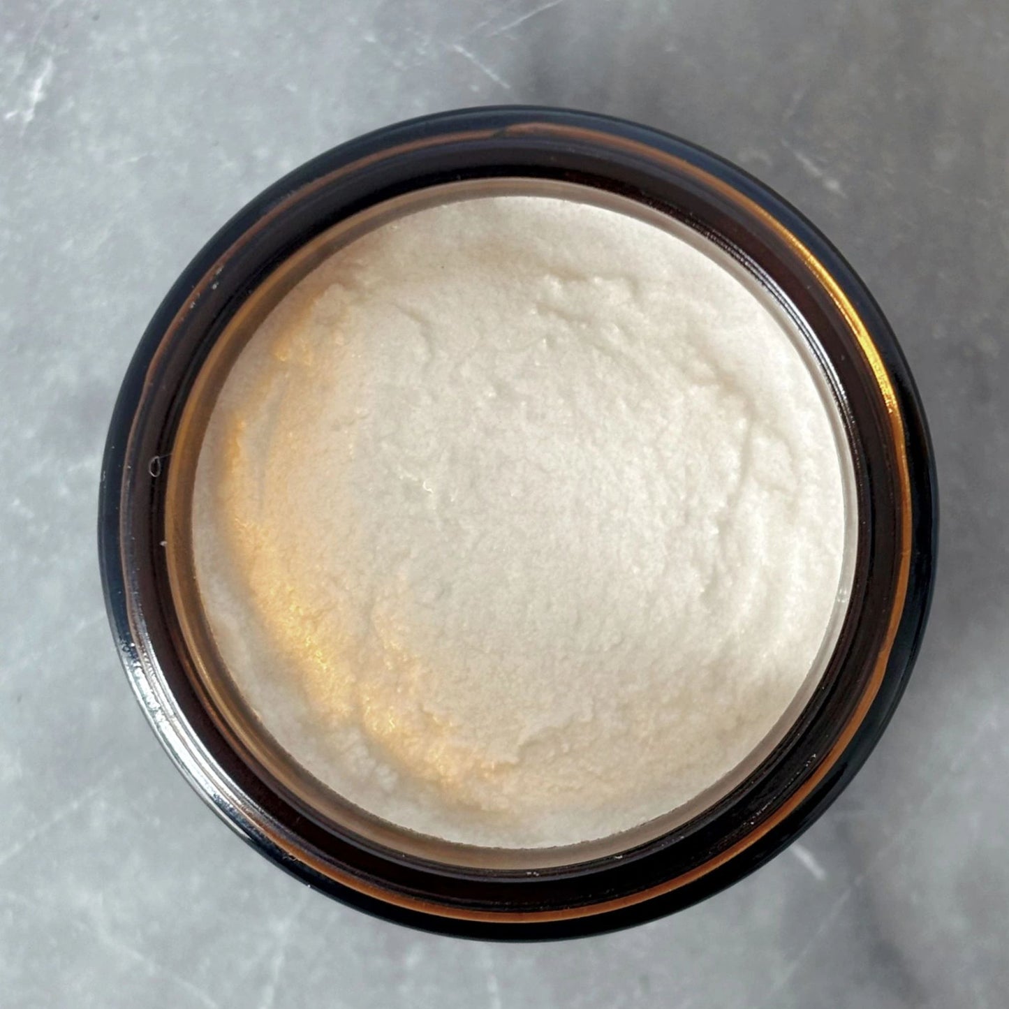 Top view of Maxwell & McIntyre Baking Soda Coconut Oil fluoride free toothpaste texture in amber glass jar on marble surface.