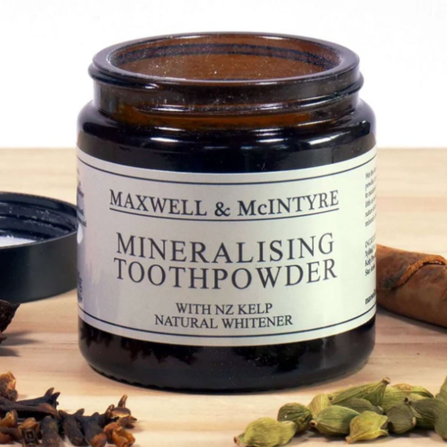 Maxwell and McIntyre Natural Organic Mineralising Toothpowder in open amber glass jar with NZ kelp natural whitener surrounded by cloves star anise cardamom and cinnamon.