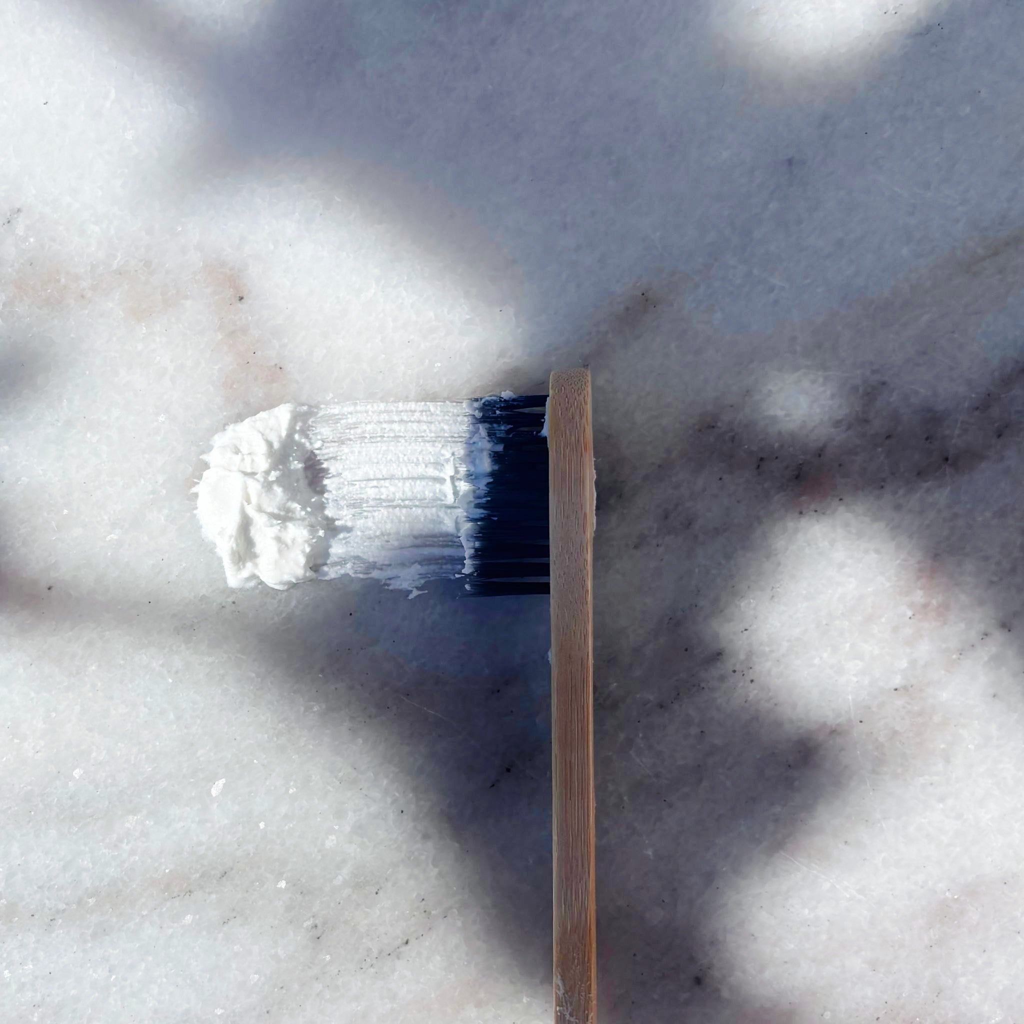Close up of Maxwell & McIntyre Coconut Oil fluoride free toothpaste on bamboo toothbrush over marble surface.
