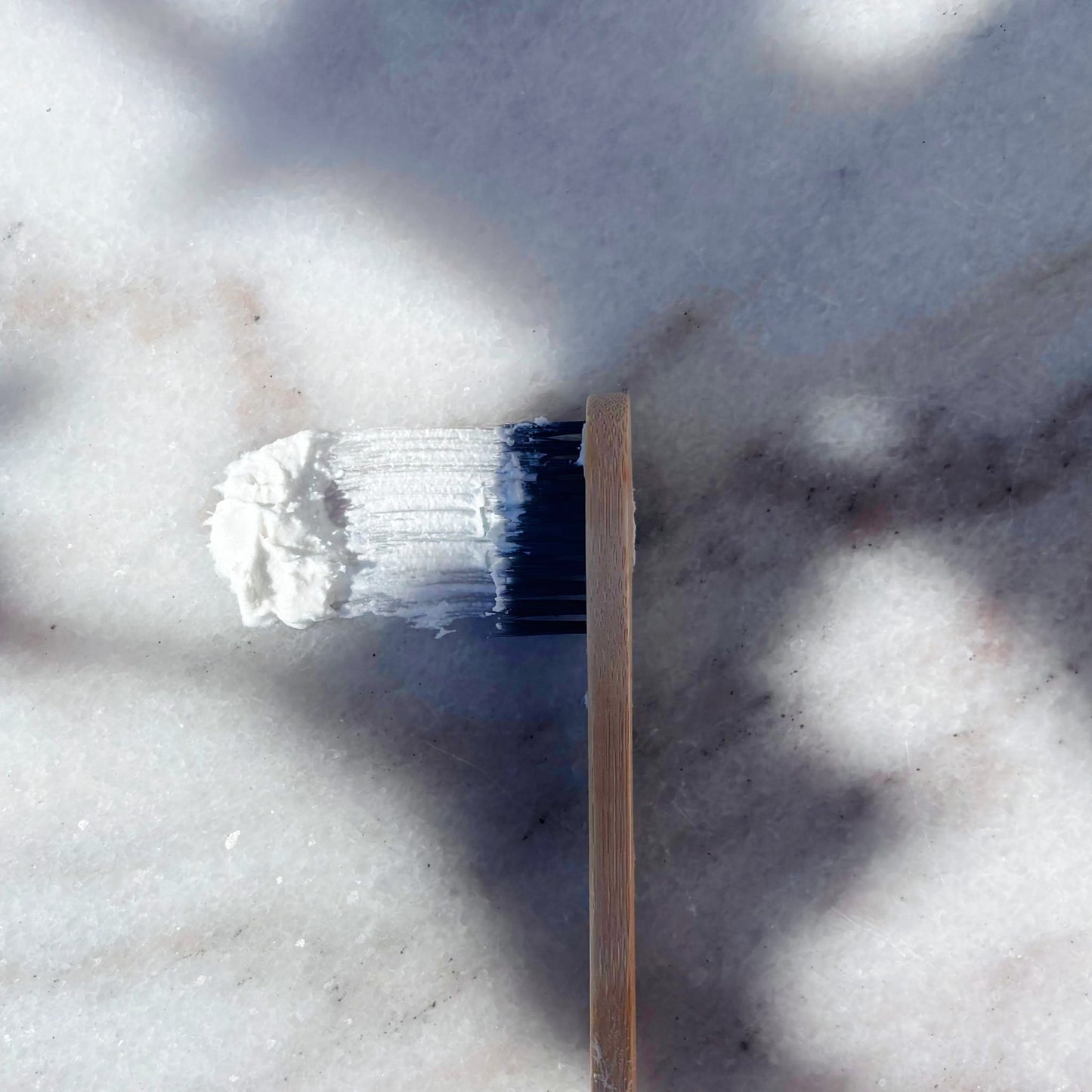 Close up of Maxwell & McIntyre Coconut Oil fluoride free toothpaste on bamboo toothbrush over marble surface.