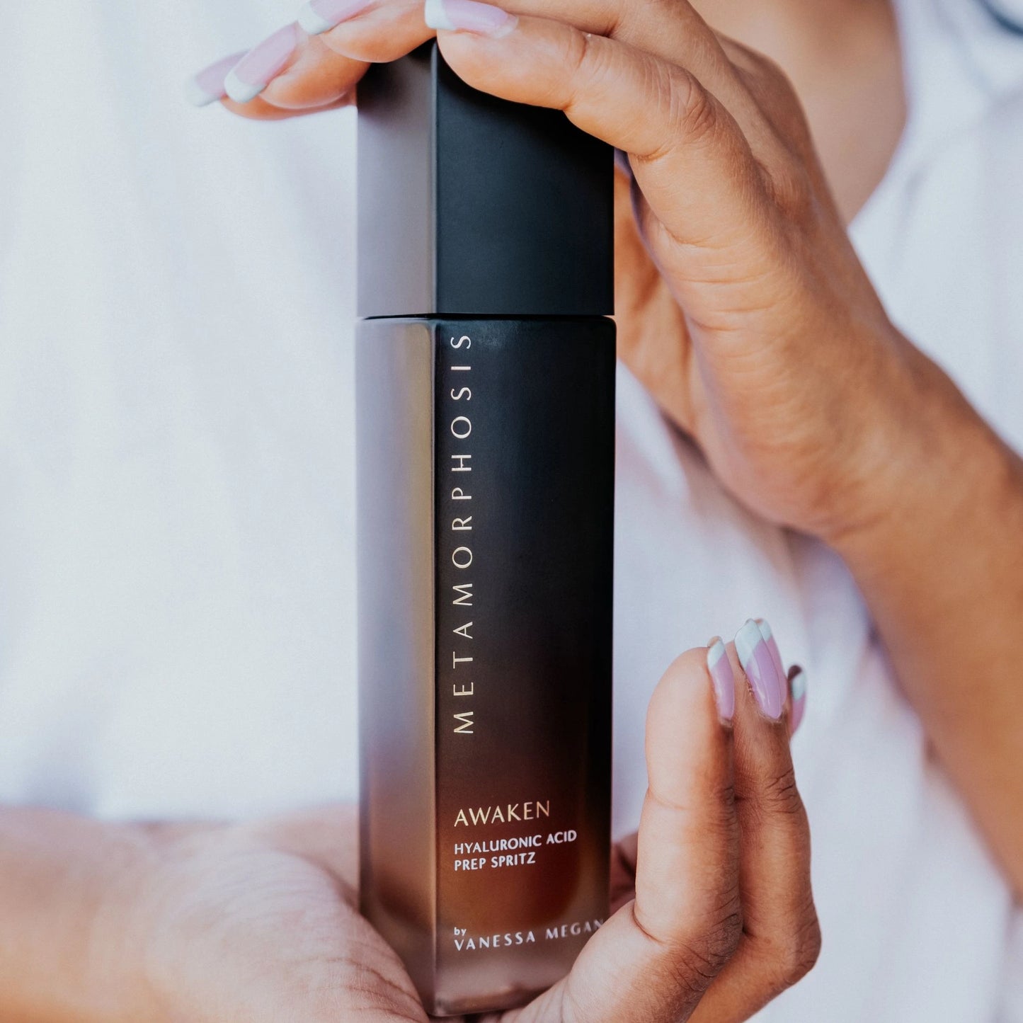 Hands gently holding the Metamorphosis Awaken Hyaluronic Acid Spritz bottle.