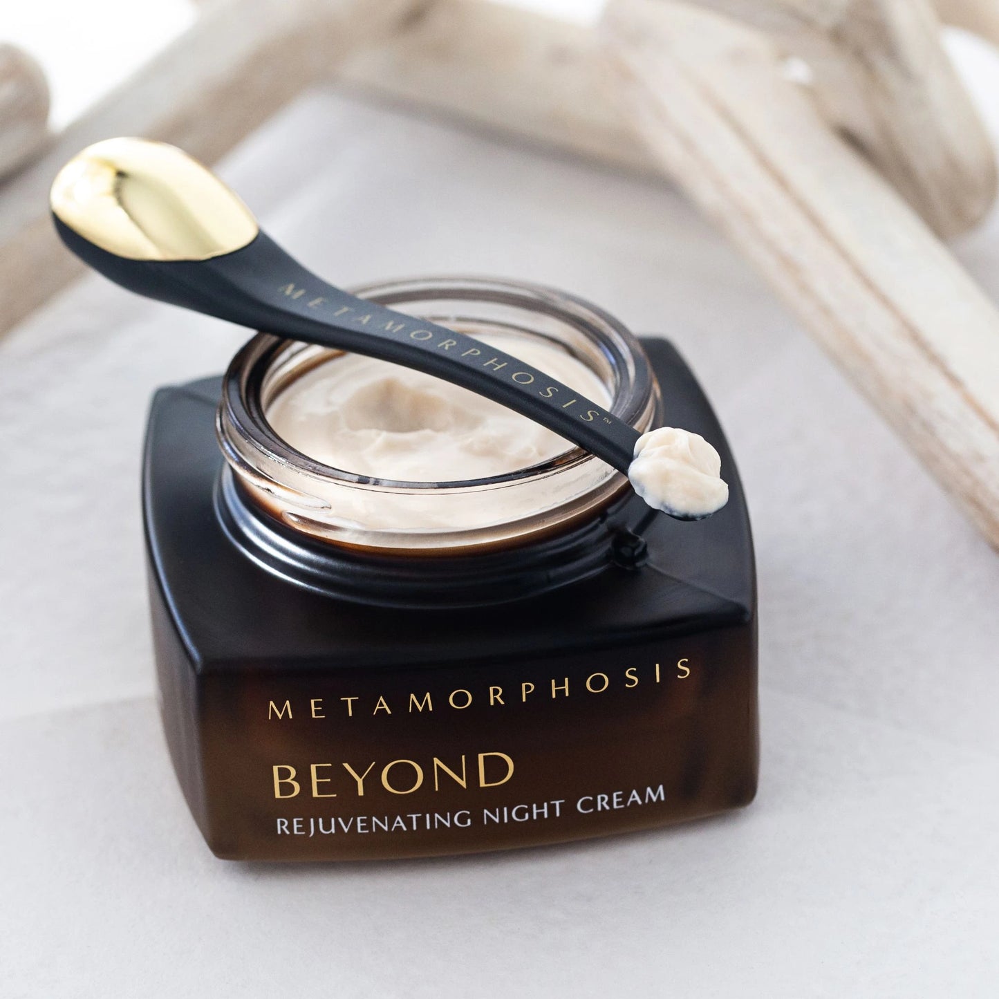 Open jar of Metamorphosis Beyond Rejuvenating Night Cream with gold-tipped spatula resting on top, showcasing the creamy, nutrient-rich natural formulation.
