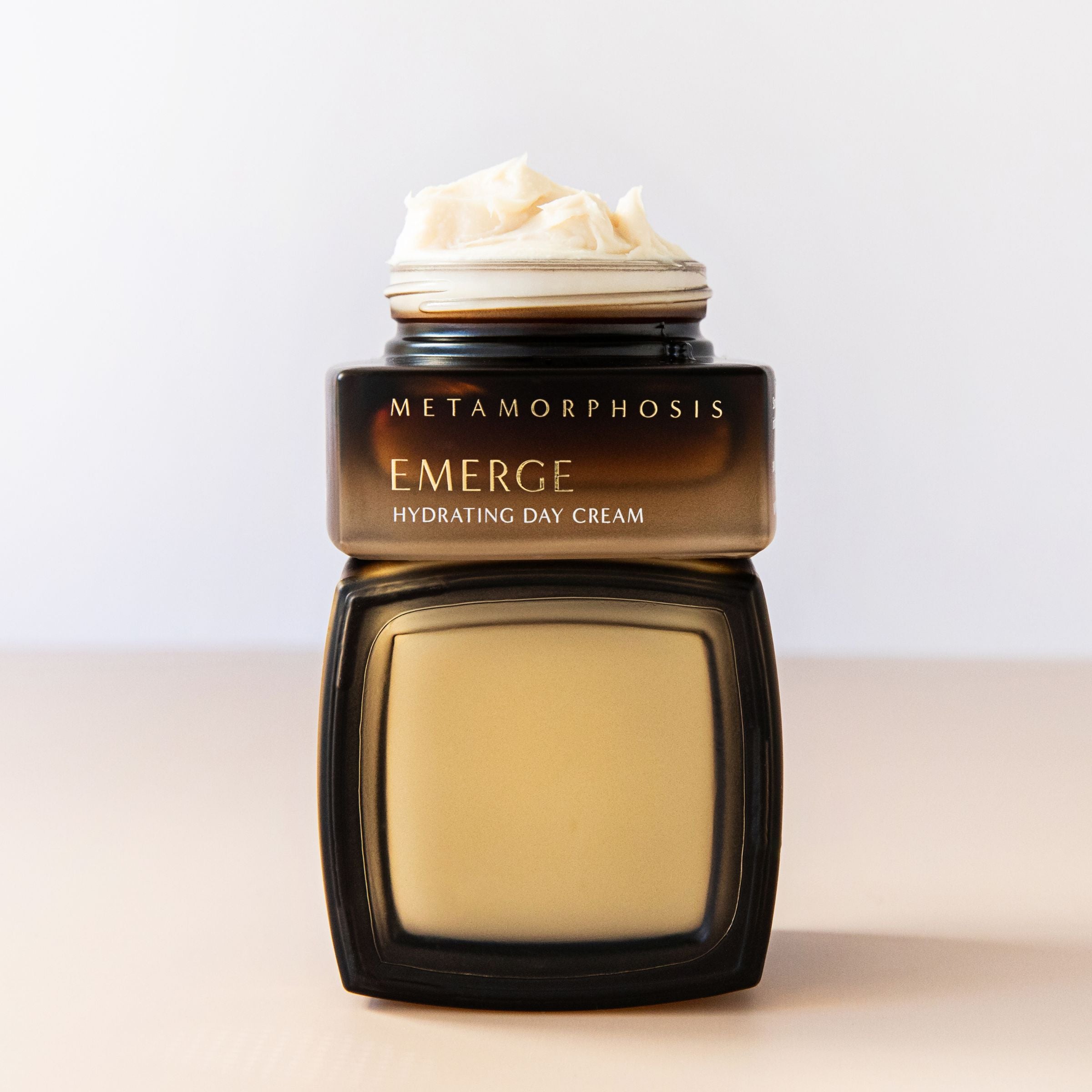 Stacked Metamorphosis Emerge Hydrating Day Cream jars, one open to reveal its rich, creamy texture. Expertly formulated and clinically proven to hydrate and protect peri to post-menopausal skin.