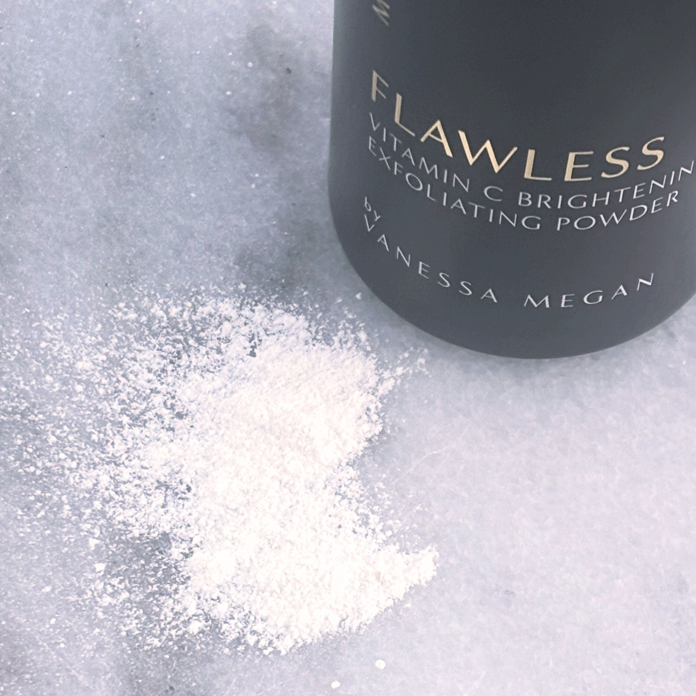 Close-up of Metamorphosis Flawless Vitamin C Brightening Exfoliating Powder by Vanessa Megan with a sprinkle of the fine, white powder displayed on a marble surface, highlighting its texture and application format.