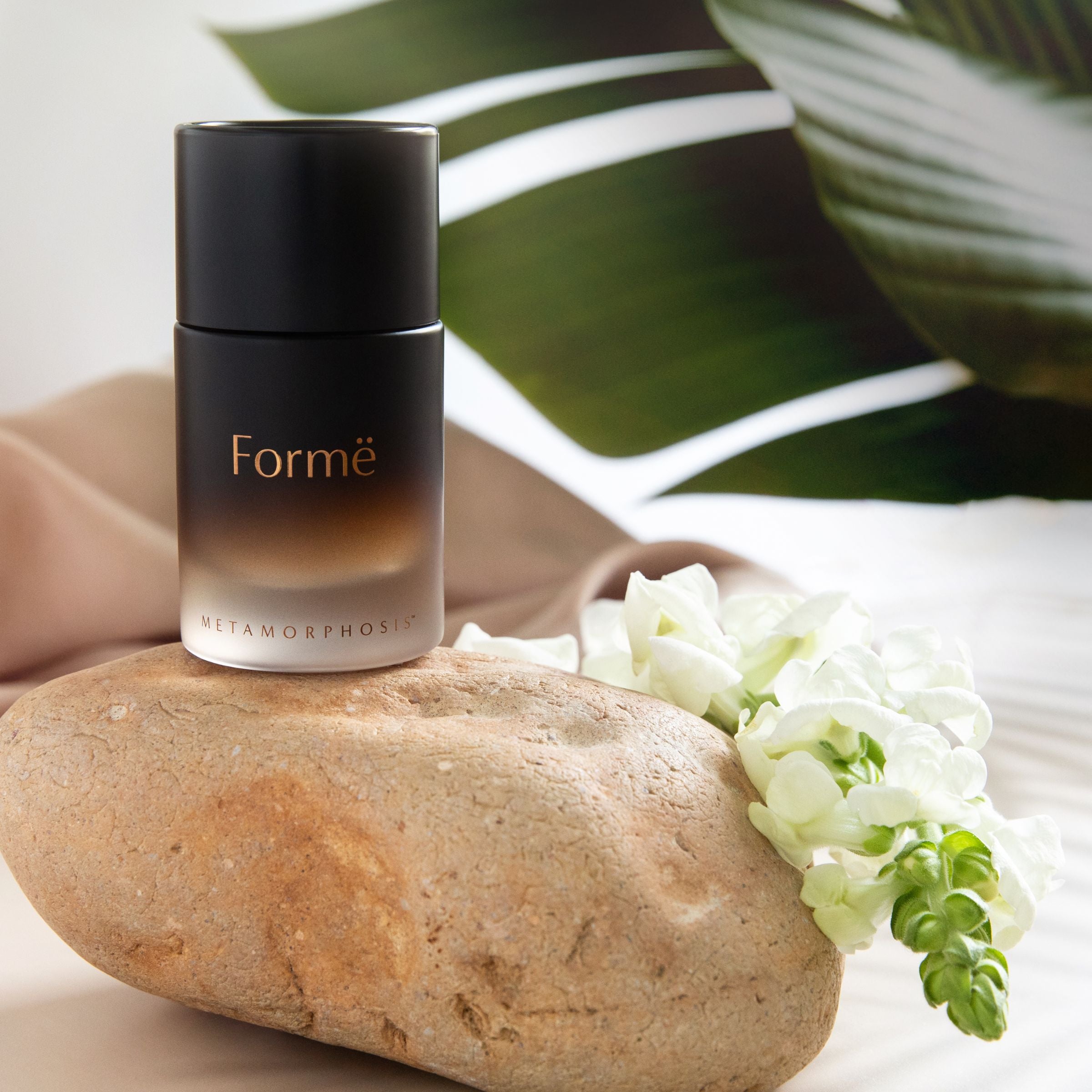 Metamorphosis Formē [for-MAY] 100% natural aromatherapeutic perfume by Vanessa Megan for hormonal balance during menopause stages, shown resting on a smooth stone with soft white snapdragons.