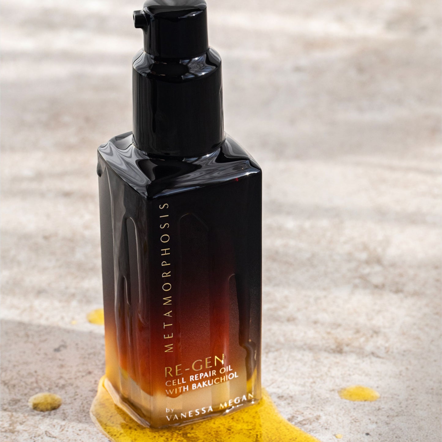 Metamorphosis Re‑Gen Cell Repair Oil with Bakuchiol by Vanessa Megan – rich golden face oil visibly spilling from sleek bottle onto stone surface, highlighting radiant skin restoration for peri‑ to post‑menopausal skin.