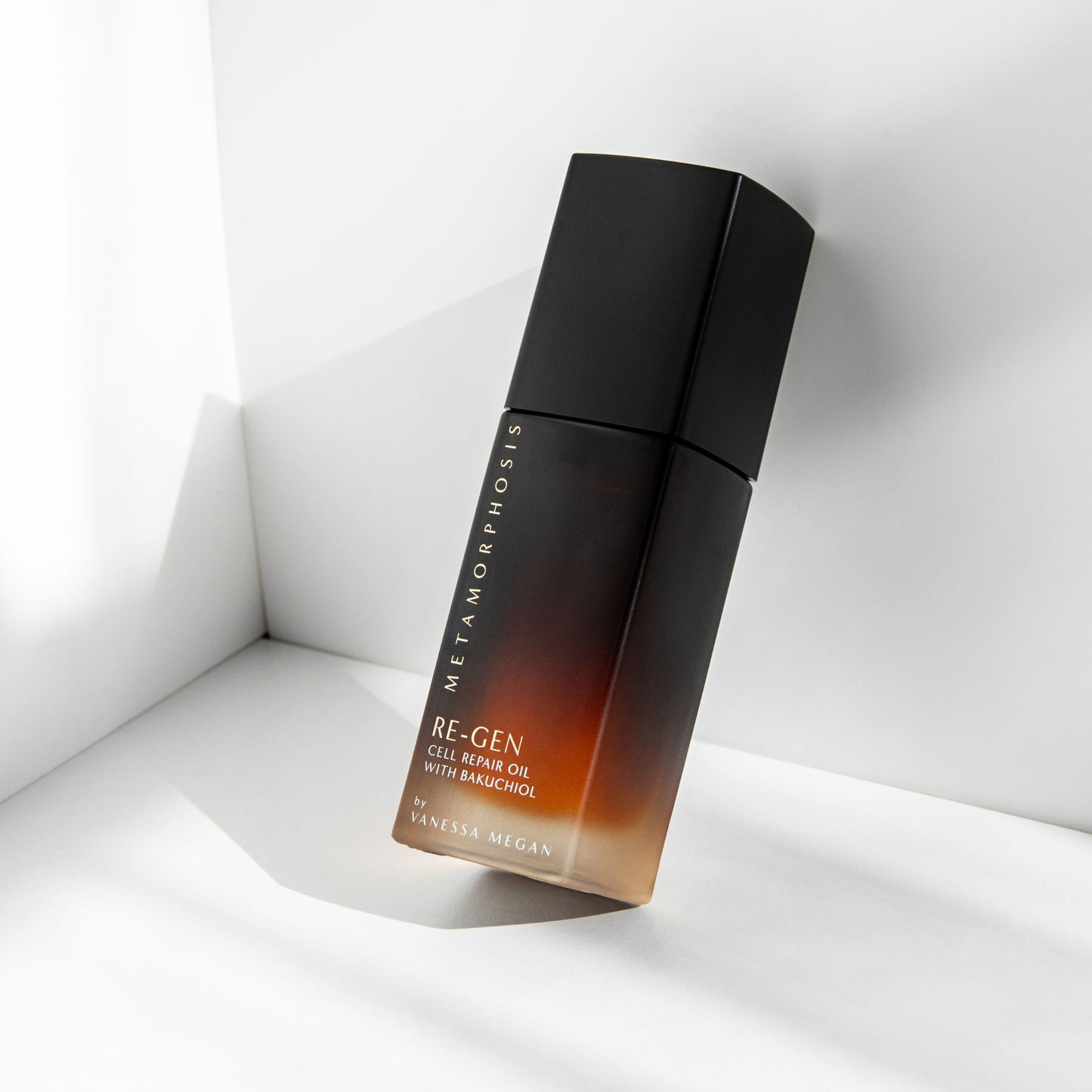 Metamorphosis Re-Gen Cell Repair Oil with Bakuchiol by Vanessa Megan, a sleek gradient amber-to-black bottle angled in sunlight against a clean white corner background.