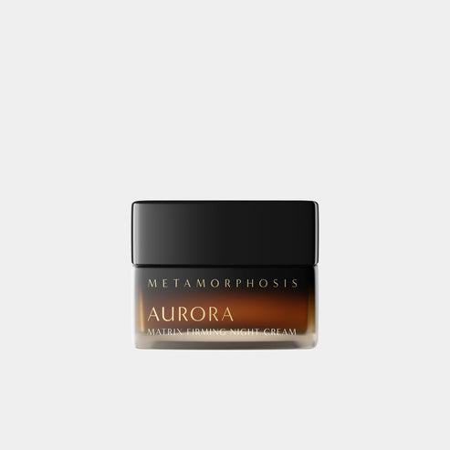 A jar of Metamorphosis Aurora Matrix Firming Night Cream, featuring a black lid and a dark amber-brown glass cosmetics jar with gold lettering, set against a solid light gray background at Intentionally Natural NZ.