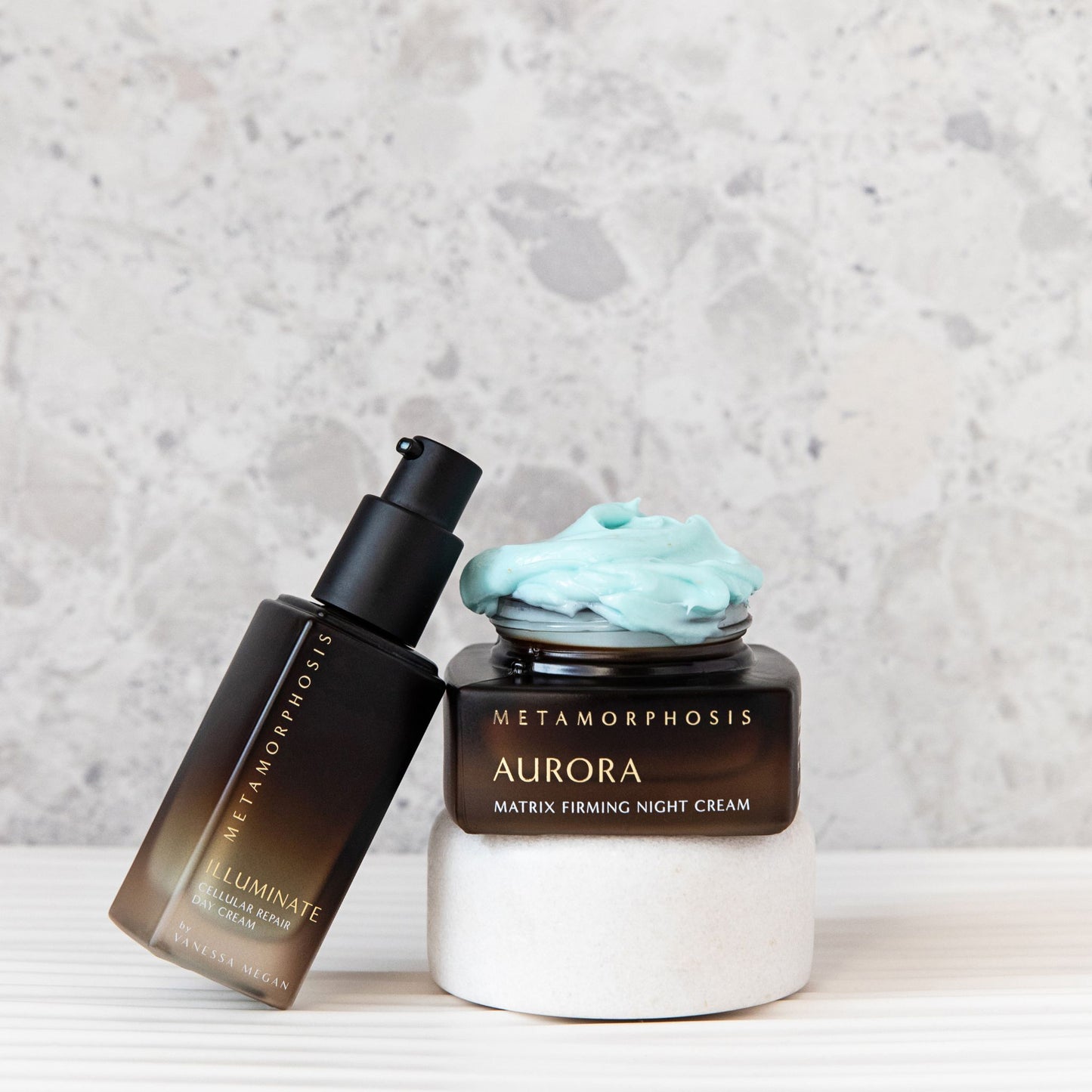 Aside by side of the open  Metamorphosis Illuminate Day cream   and the Metamorphosis Aurora Matrix Night Cream  with the cream spilling over the top of the jar in natural light.