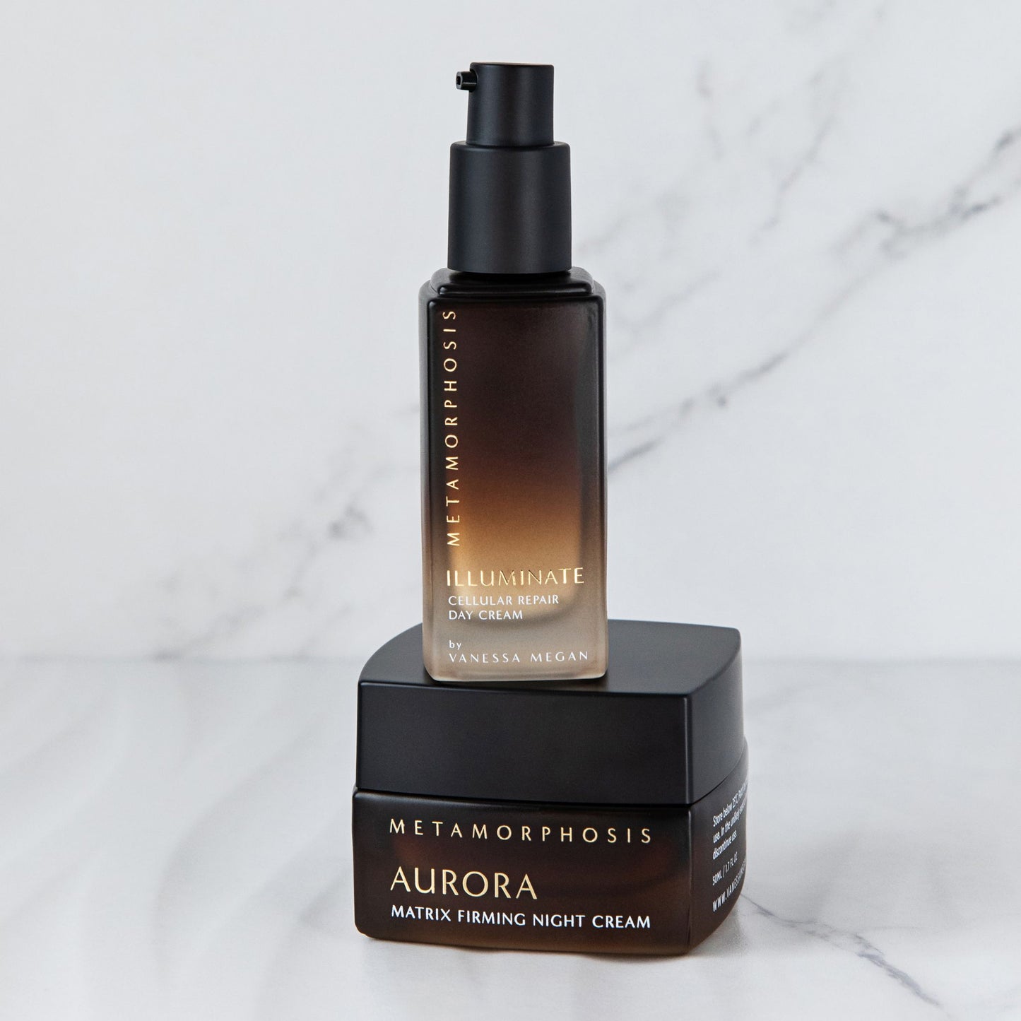 A bottle of Metamorphosis Skincare Illuminate Cellular Repair Day Cream standing on top of the Metamorphosis Skincare Aurora Matrix fFirming Night Cream in fornt of a marbal background.