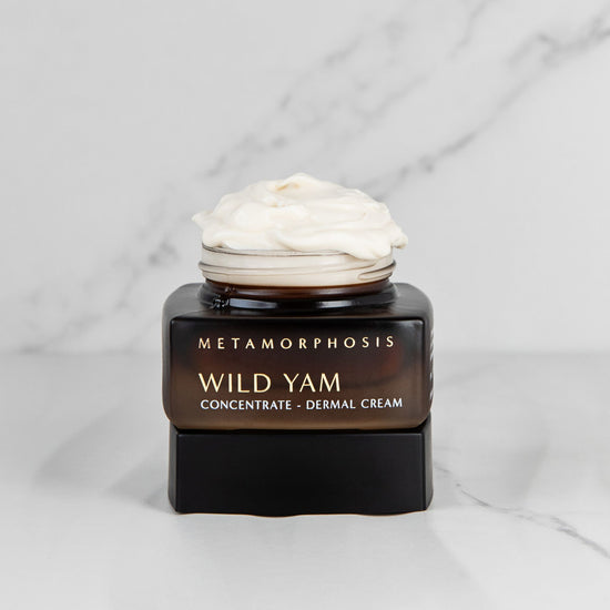 Metamorphosis Skincare Wild Yam Concentrate Dermal Cream jar open on lid with cream  over flowing over the jar on a marble background.