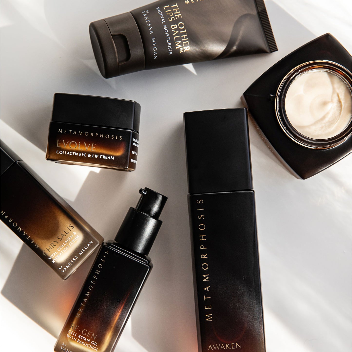 Flat lay of Metamorphosis skincare range by Vanessa Megan including The Other Lips Balm, Evolve Collagen Eye & Lip Cream, Chrysalis Collagen Crème, Re-Gen Cell Repair Oil, Awaken Cleanser, and face cream – formulated for peri to post-menopausal skin.