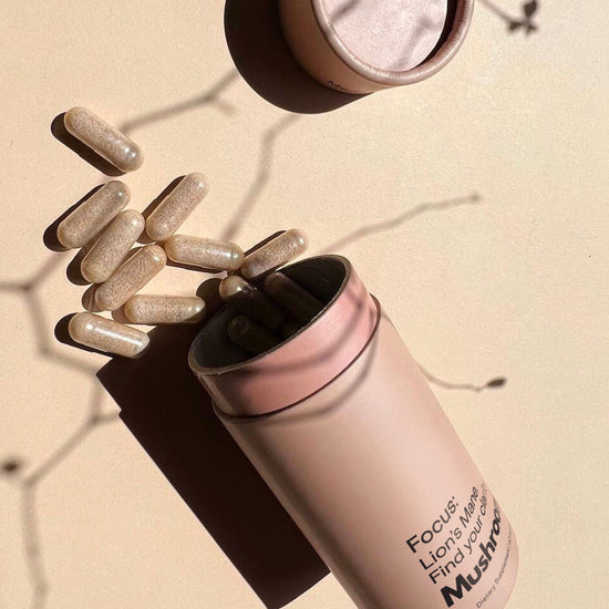 Mother Made Focus Lion’s Mane capsules spilled from BPA-free recyclable packaging onto a soft neutral surface with natural light and shadows.