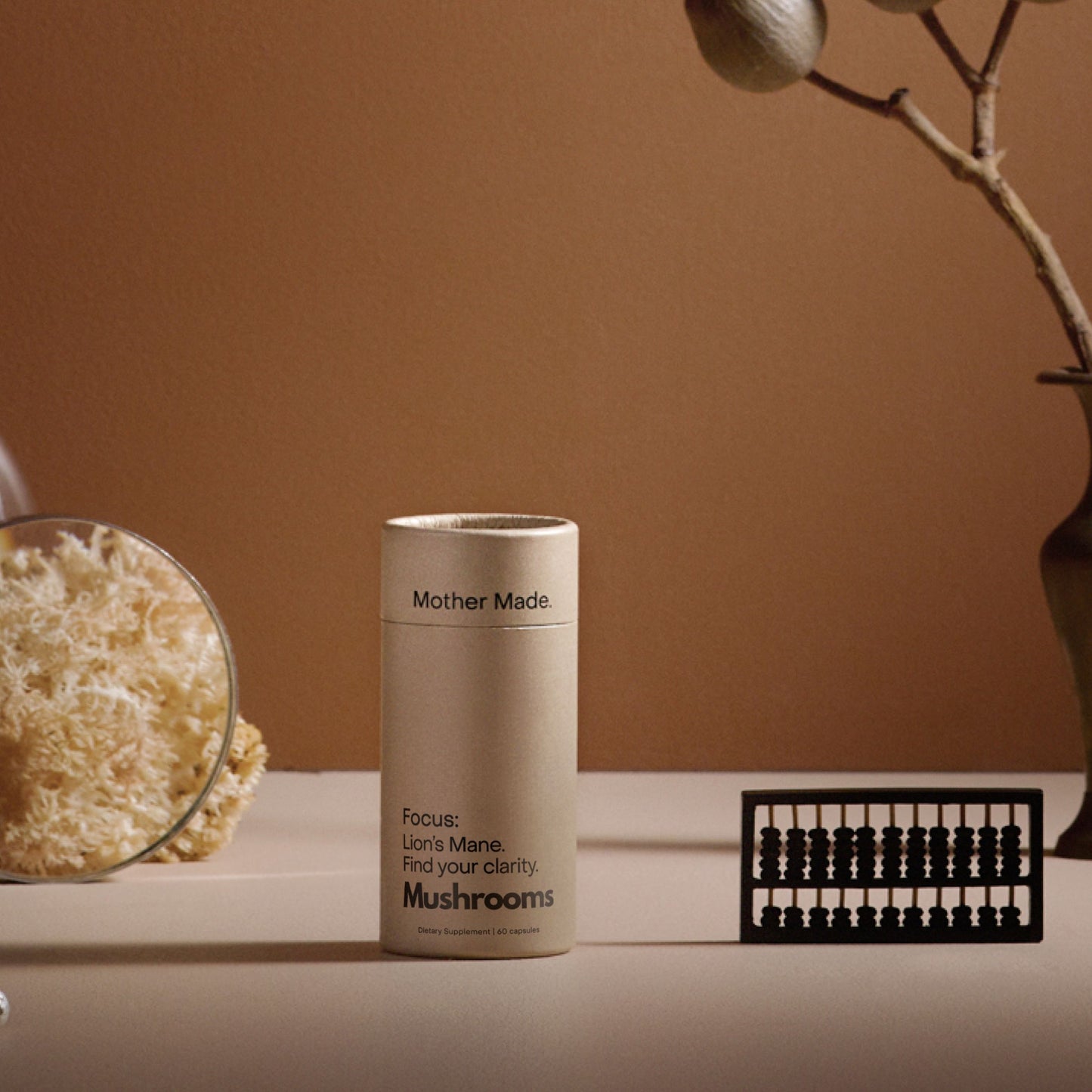 Mother Made Focus Lion’s Mane mushroom supplement in BPA-free recyclable packaging, styled with dried botanicals and magnified Lion’s Mane.