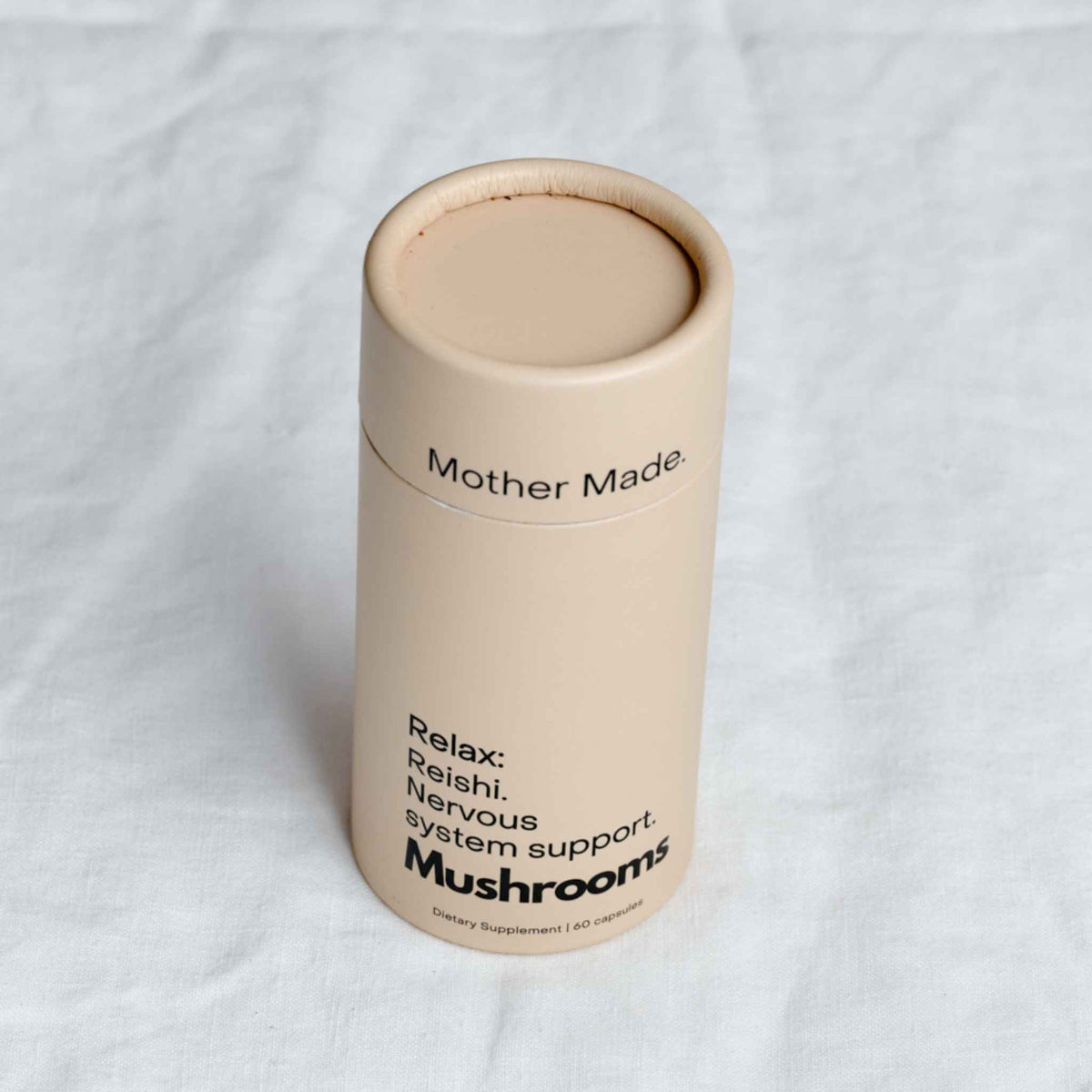 Mother Made Relax Reishi Capsules in a recyclable cardboard canister on a linen tablecloth, a mushroom supplement for nervous system support