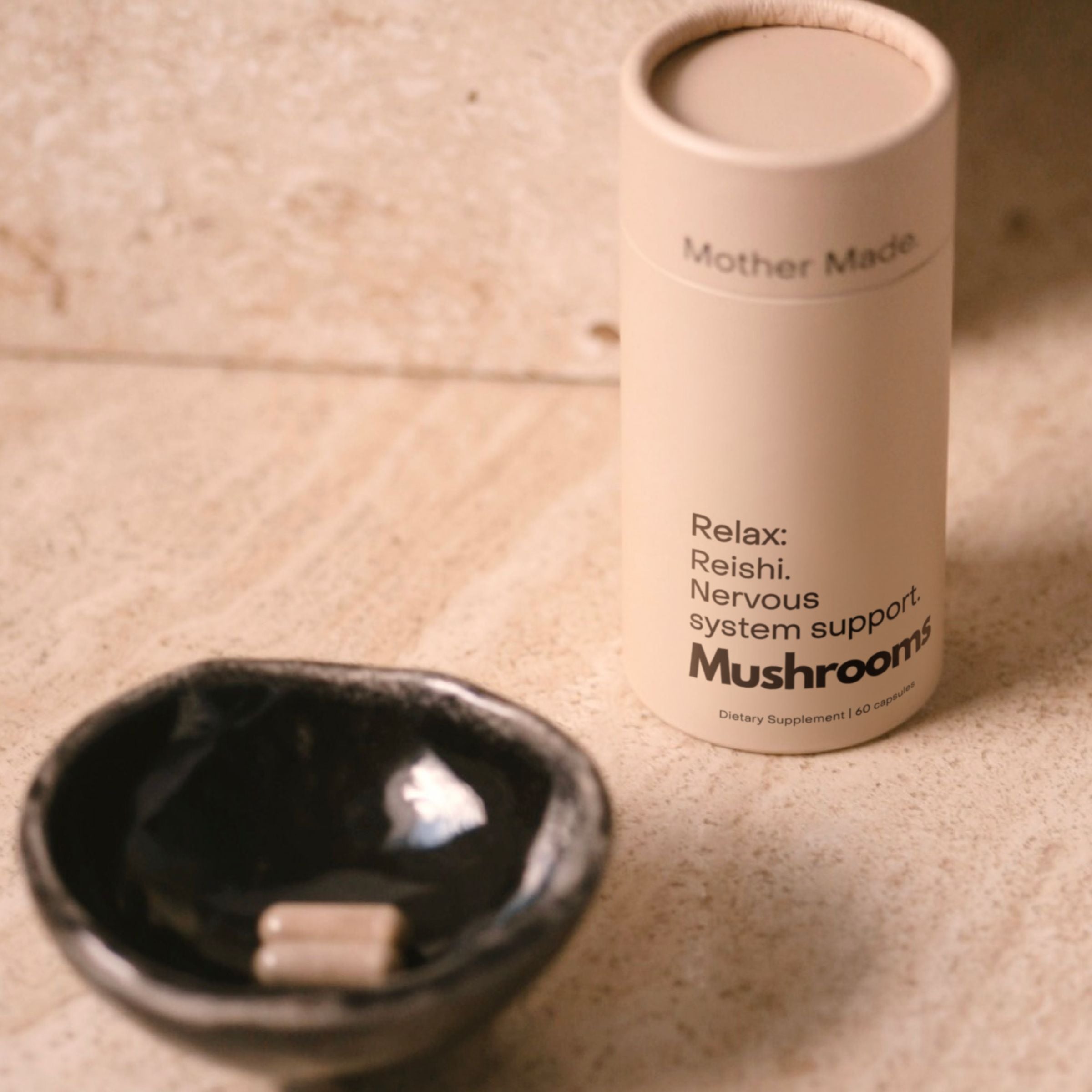 Mother Made Reishi mushroom capsules beside a ceramic dish.