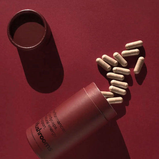 Open Mother Made Cordyceps mushroom supplement on a red surface, with capsules spilled out