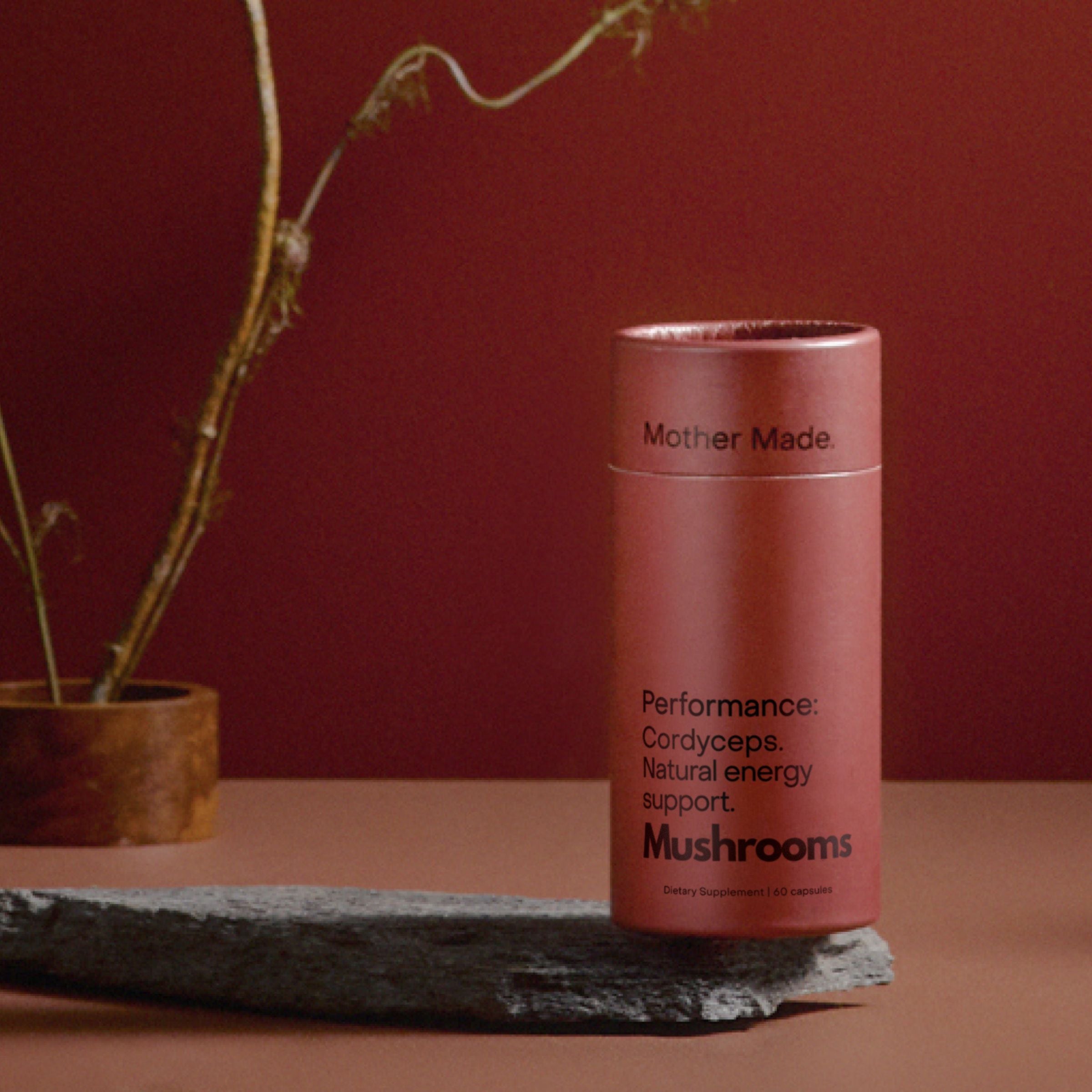 Mother Made Cordyceps mushroom supplement for performance and energy, in BPA-free recyclable packaging, styled on stone with a warm red background