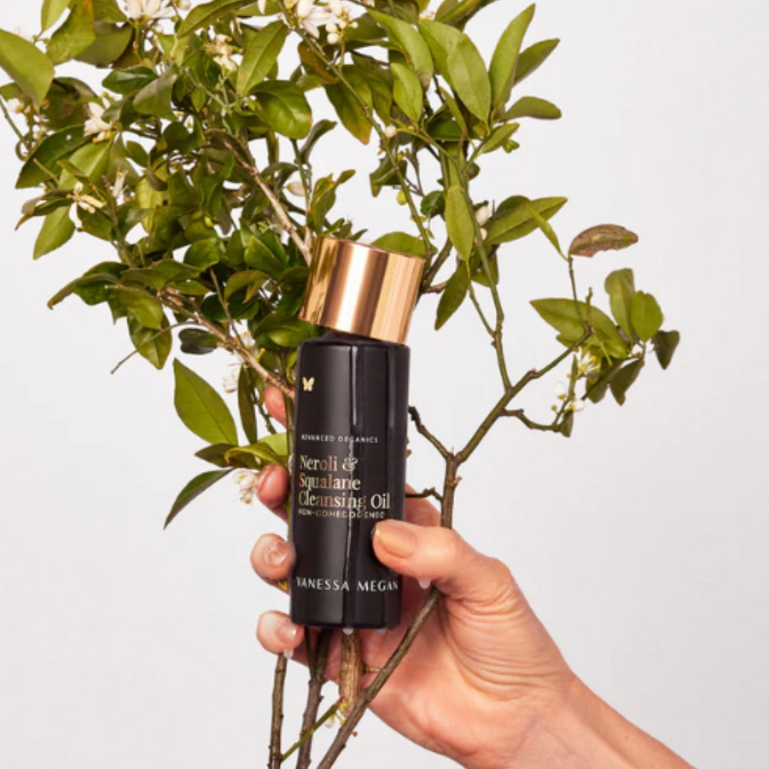 Vanessa Megan Neroli and Squalane Cleansing Oil held in hand in front of neroli tree branches.