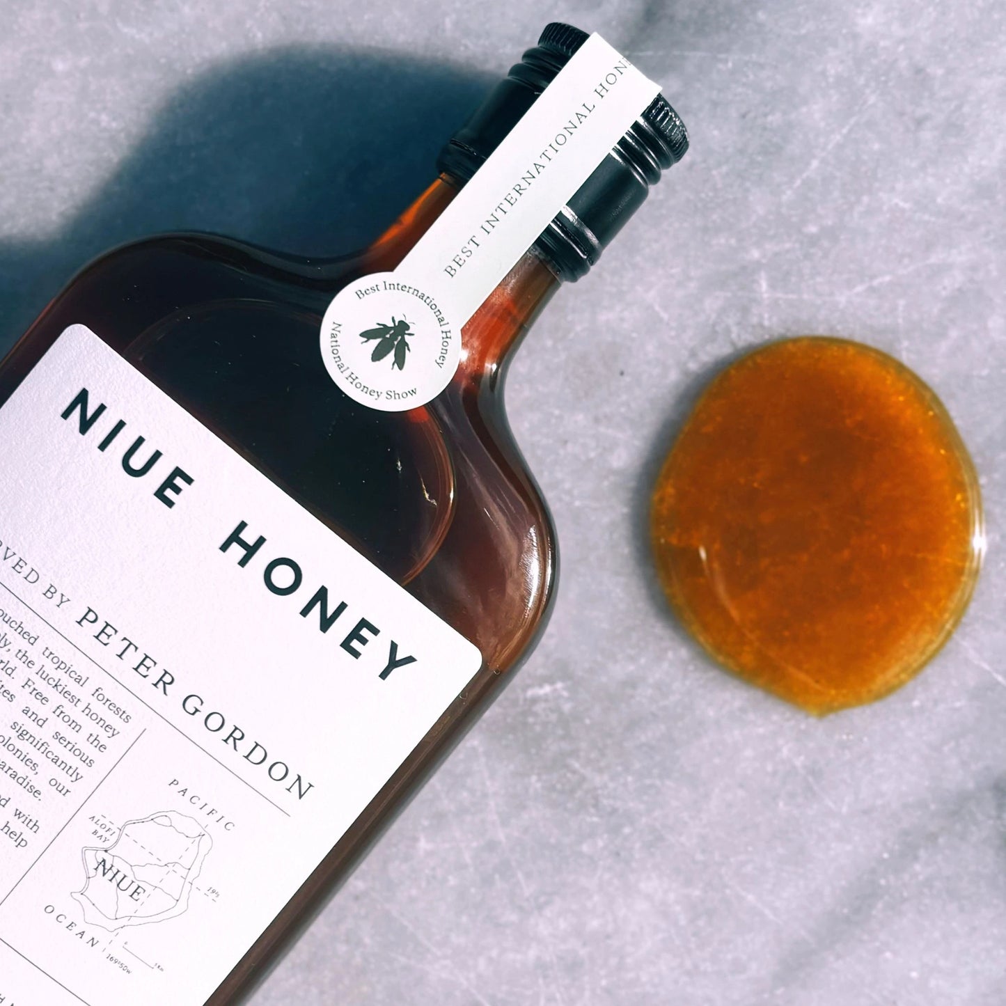 Niue Honey organic raw honey with award badge and golden honey drop on marble surface.
