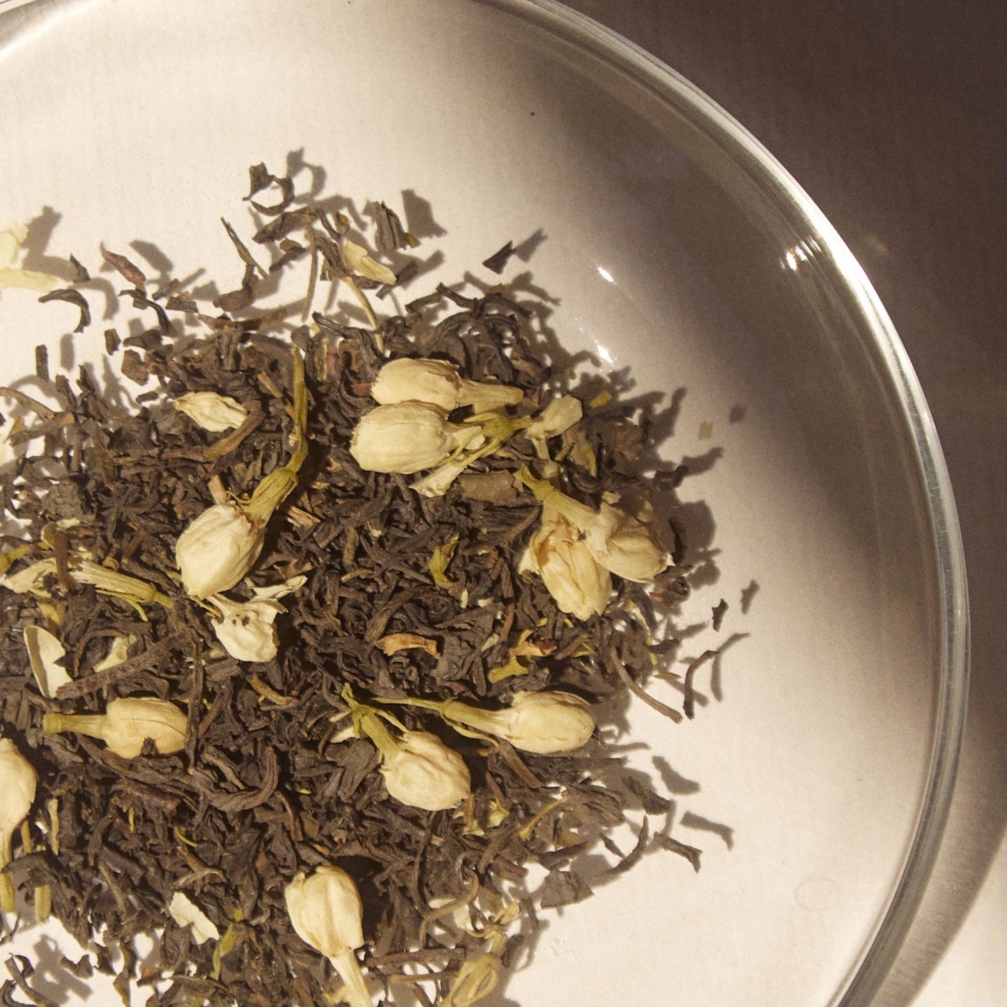 On Sundays Loose leaf blend of  the organic jasmine flowers and premium green tea leaves in a glass dish, highlighting the purity and natural composition of On Sundays Green Jasmine Tea.