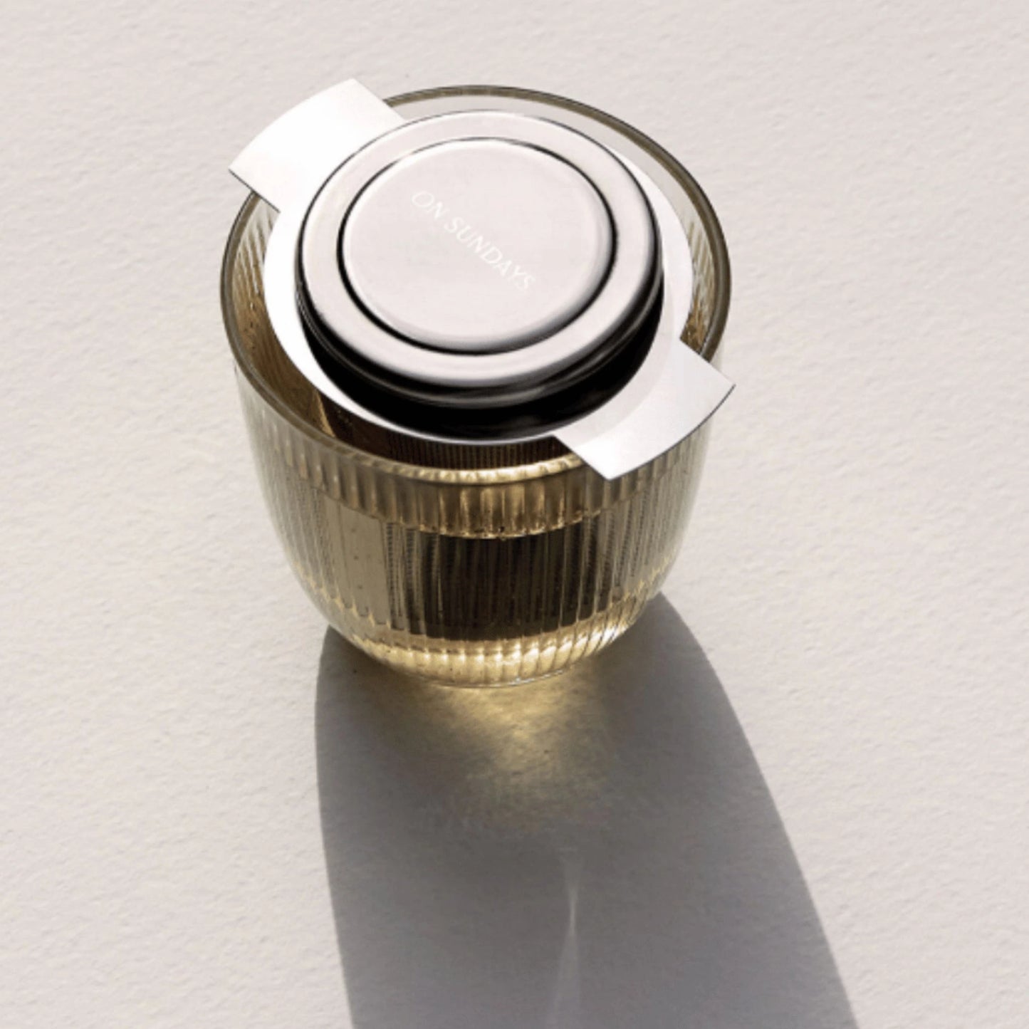 On Sundays tea infuser steeping herbal loose leaf tea in a clear ribbed glass mug with lid on top.