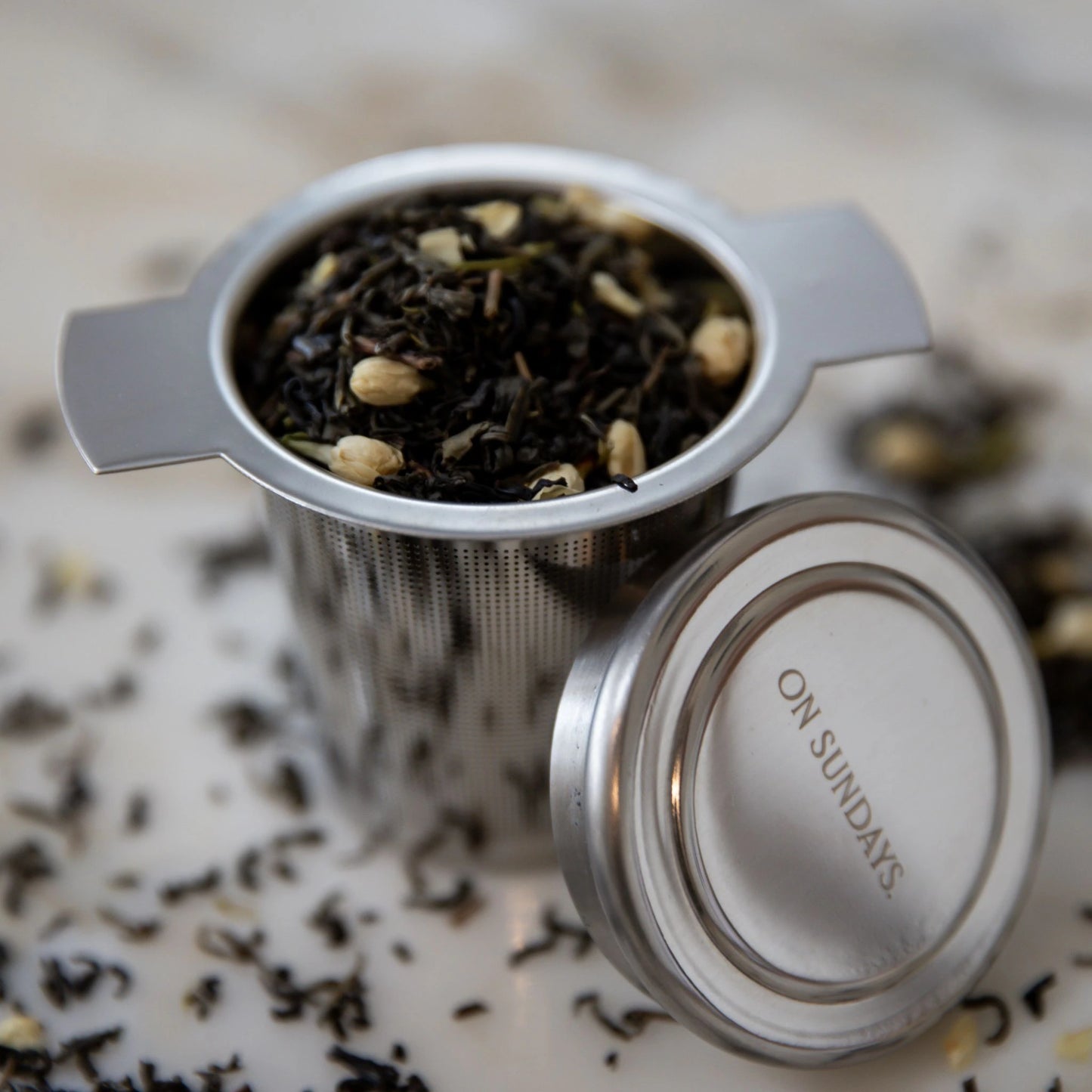 Reusable On Sundays stainless steel tea infuser filled with green jasmine tea leaves and dried jasmine buds.