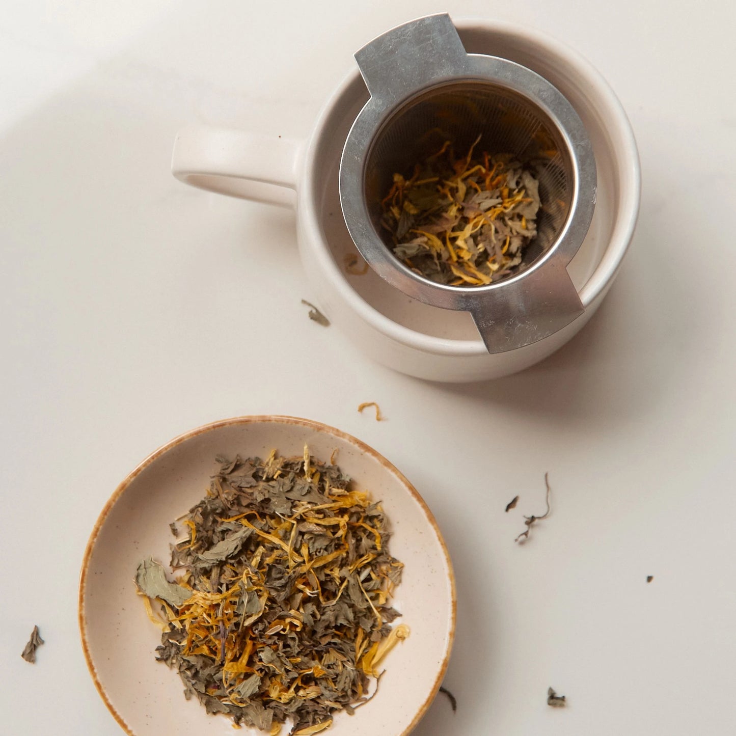 On Sundays stainless steel tea infuser set inside a ceramic mug next to a dish of the Ease tea blend.