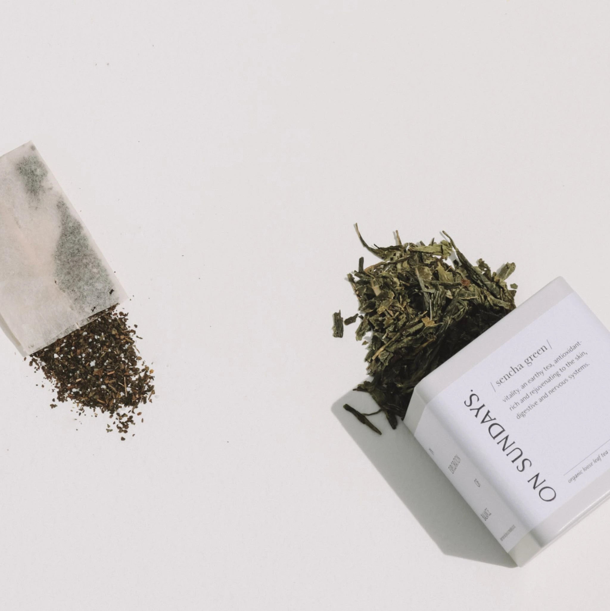Side-by-side quality comparison of On Sundays Loose leaf organic Sencha Green Tea tin beside a filled green tea generic brand tea bag.